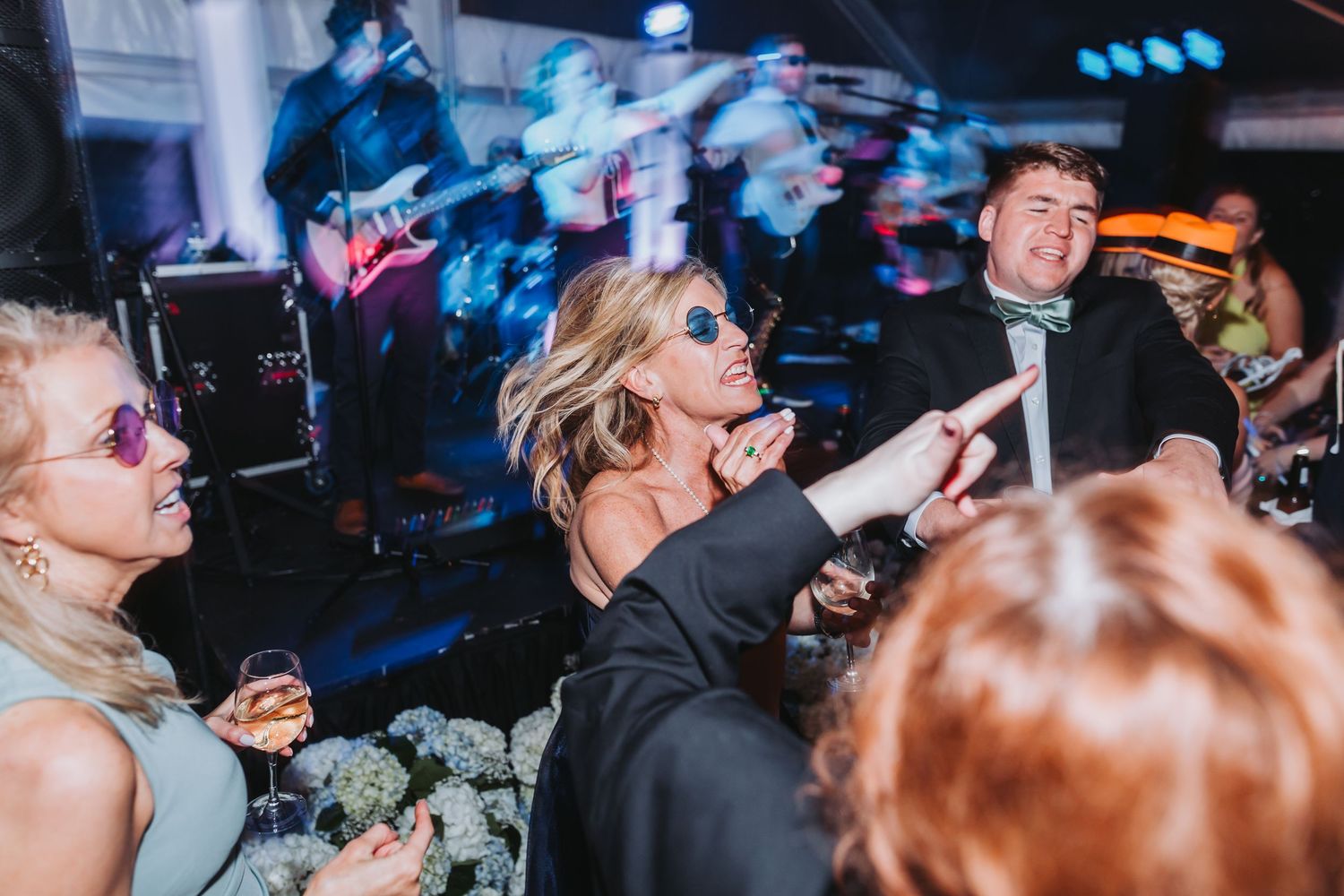 Guests dancing energetically at lively wedding reception with live band performing in background.