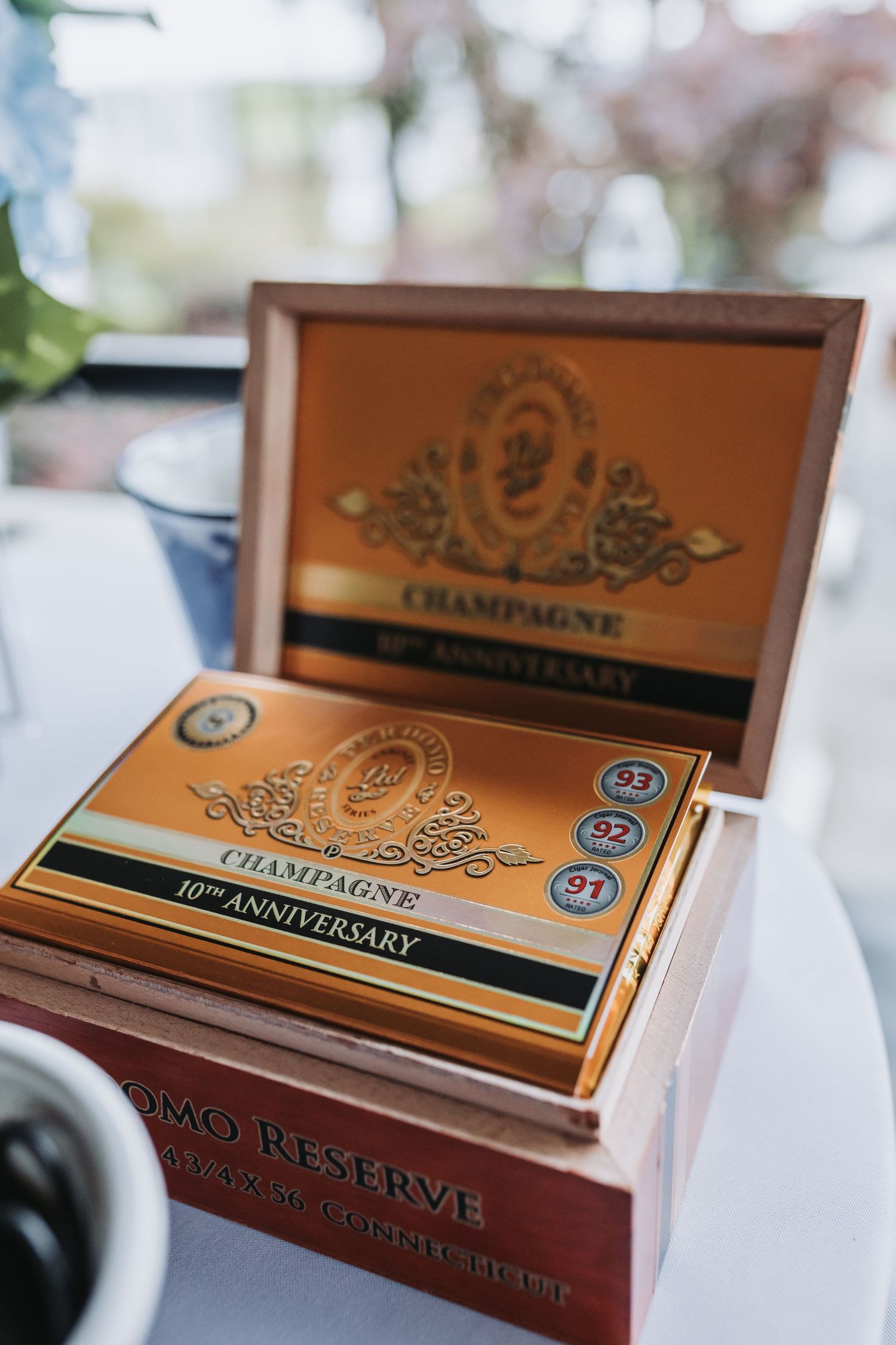 A Champagne 10th Anniversary cigar box with gold detailing displayed open on a white table at an event.