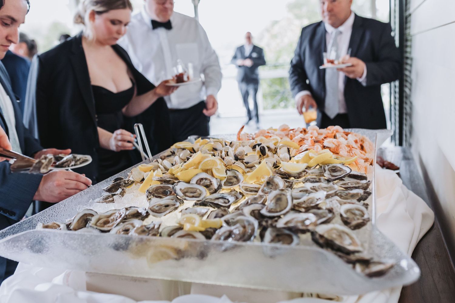 Elegant wedding cocktail hour oyster bar with guests serving themselves fresh shellfish on ice.