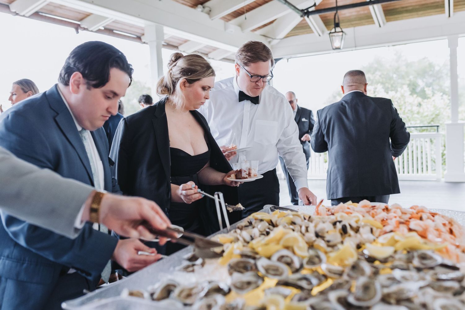 Wedding guests serve themselves at an elegant seafood buffet featuring oysters and shrimp.