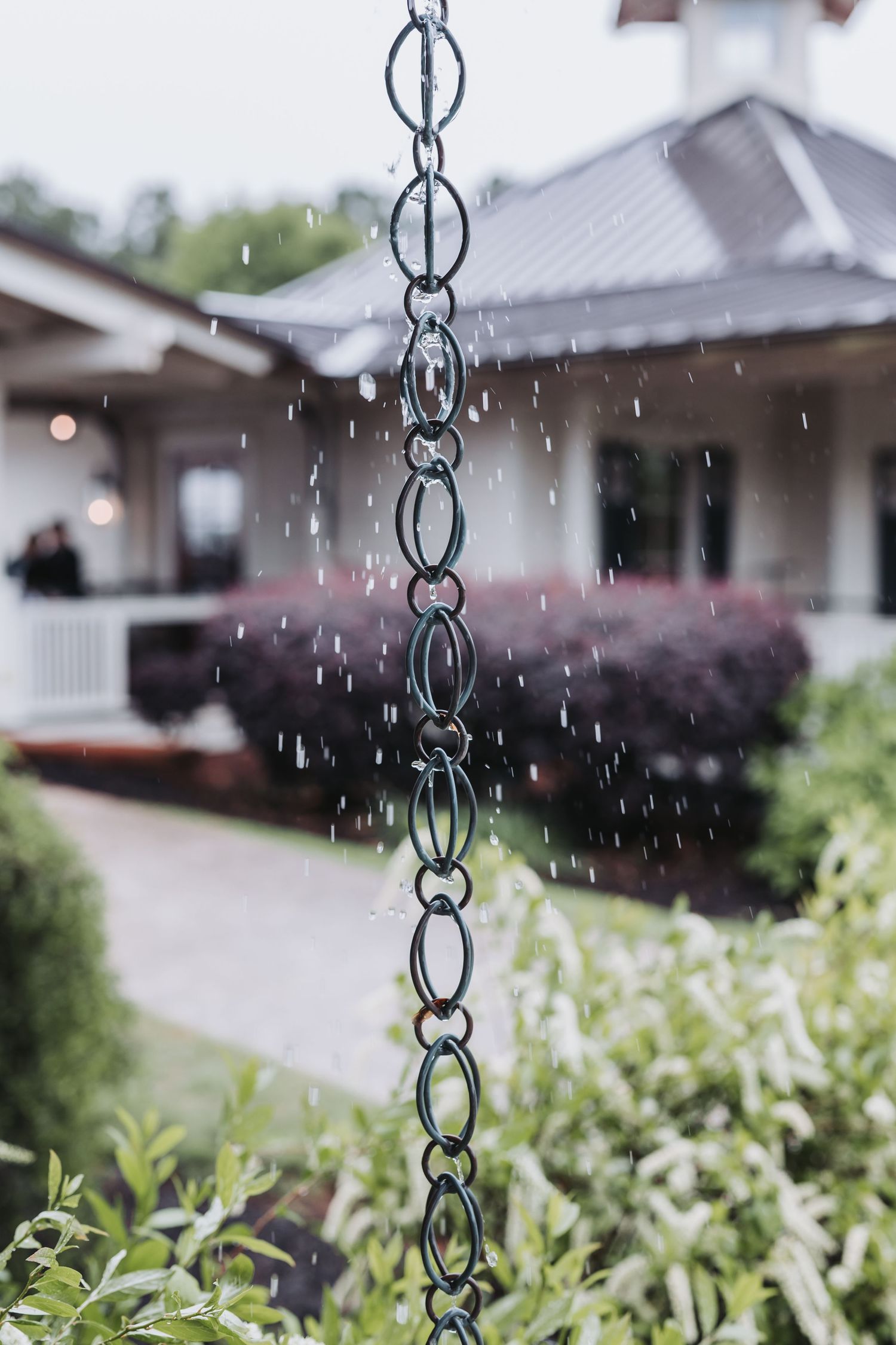 A decorative rain chain with water droplets falling during a rainy day at a wedding venue.