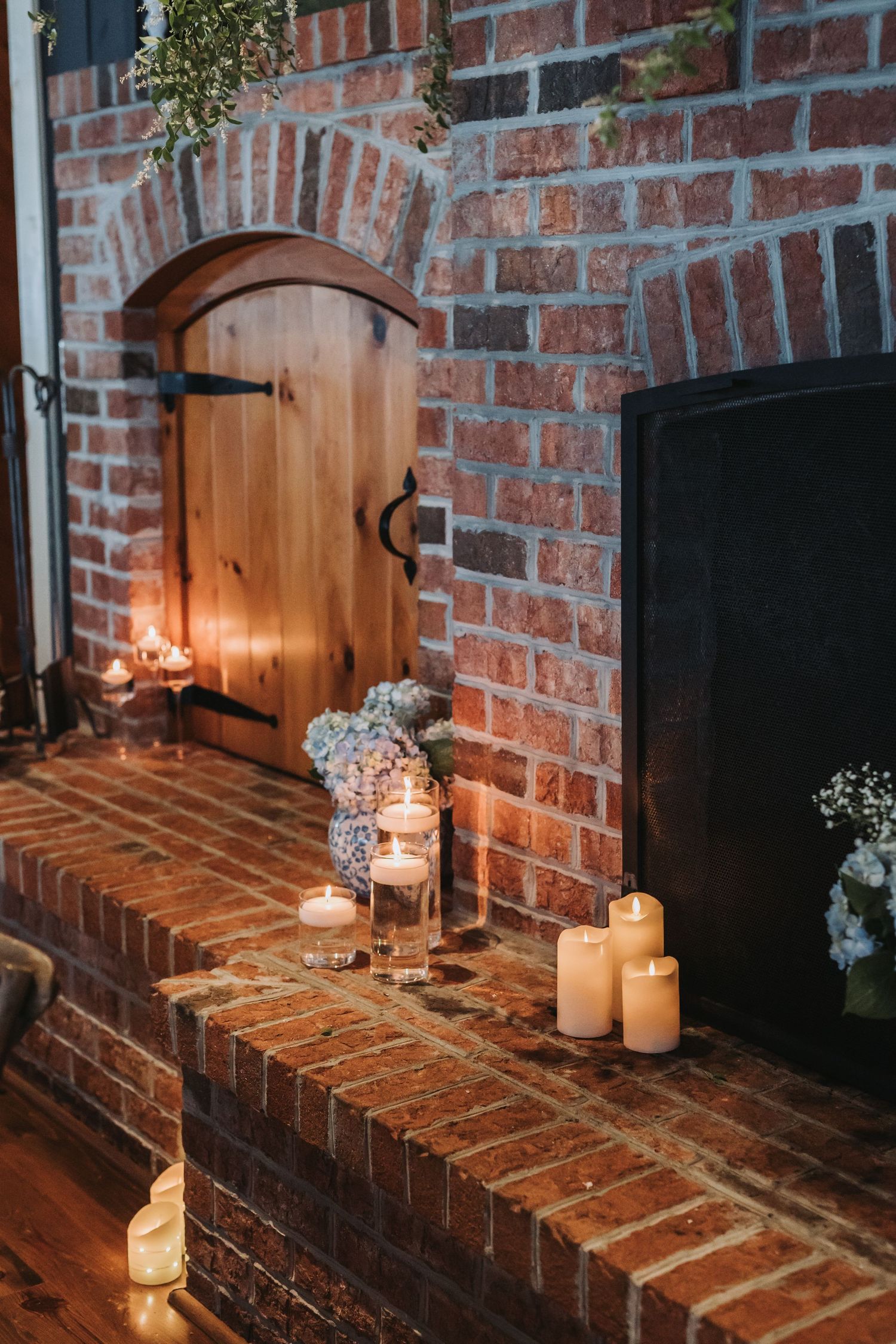 Romantic brick fireplace decorated with white pillar candles and baby's breath flowers for a wedding reception.
