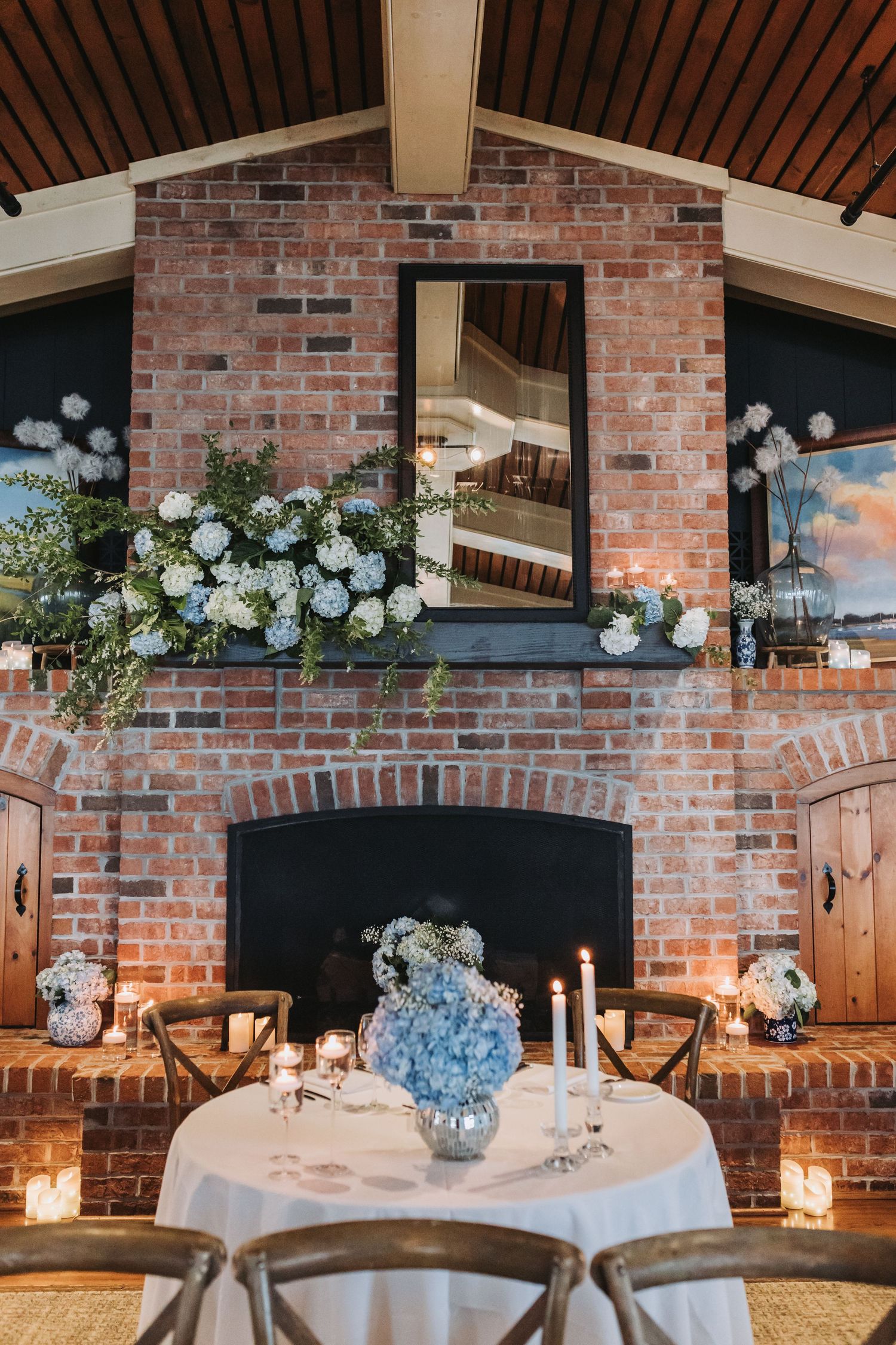 Romantic wedding sweetheart table set before a brick fireplace adorned with blue and white hydrangea floral arrangements.