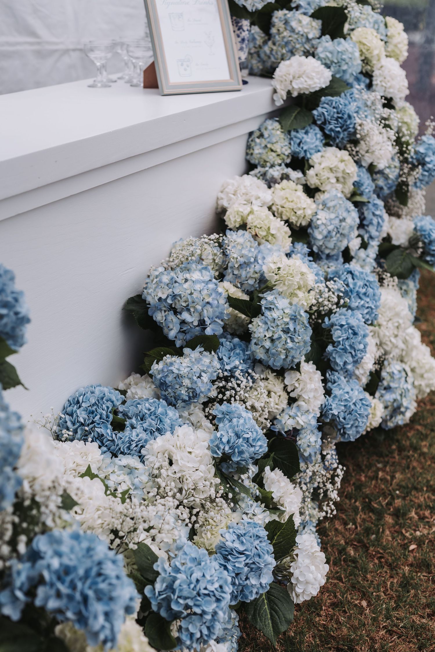 Elegant blue and white hydrangea floral arrangements cascading along a white table at a wedding reception.