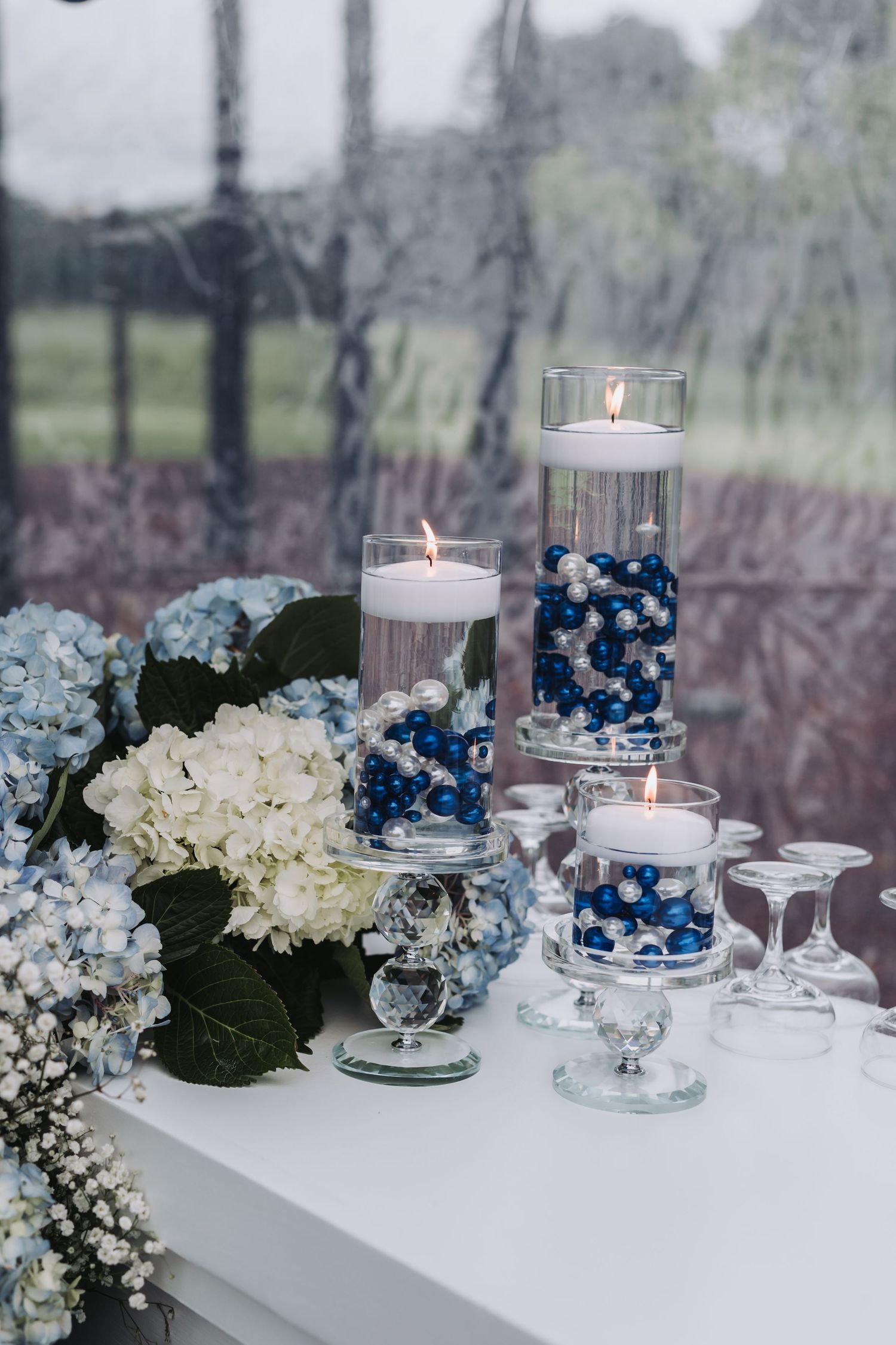 Elegant wedding centerpiece with floating candles, blue pearl vases, and white and blue hydrangea arrangements.
