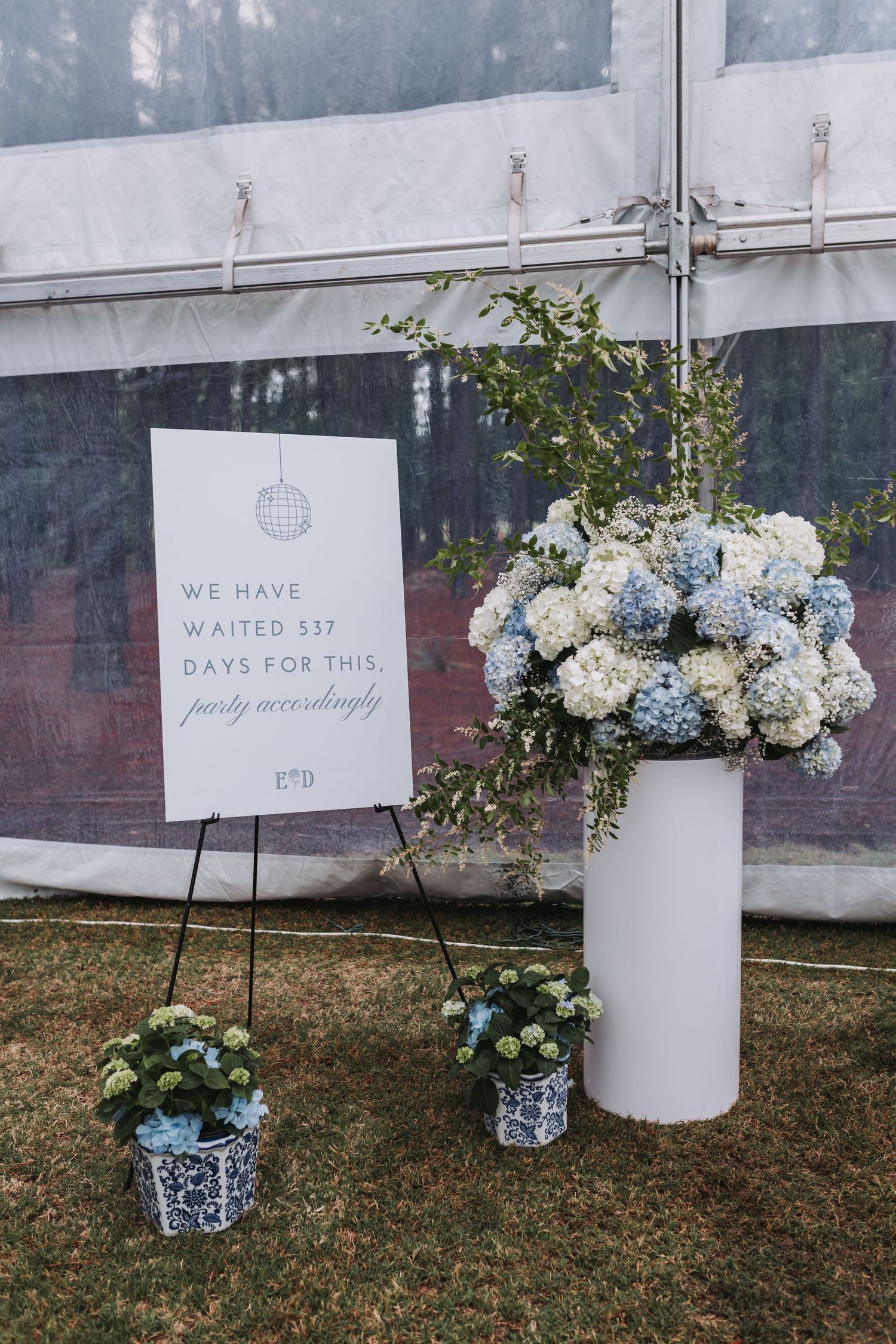 Wedding sign reading we have waited 537 days for this party with blue hydrangea floral arrangements.