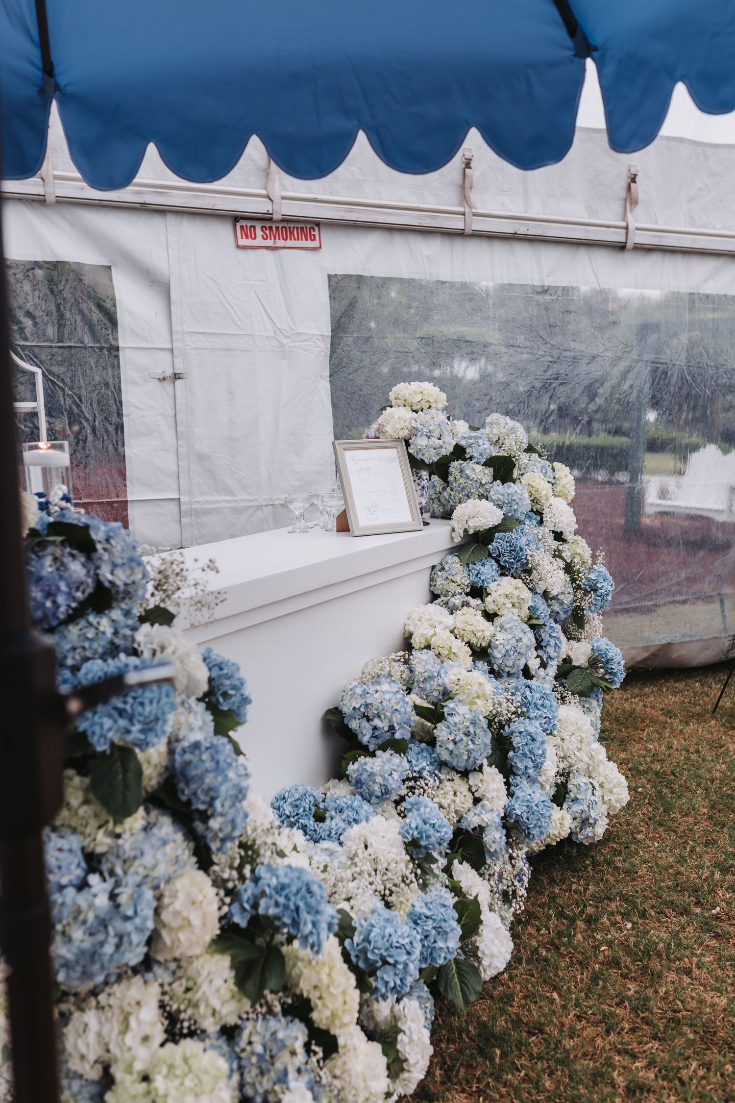 White ceremony altar adorned with lush blue and white hydrangea floral arrangements under a striped tent.