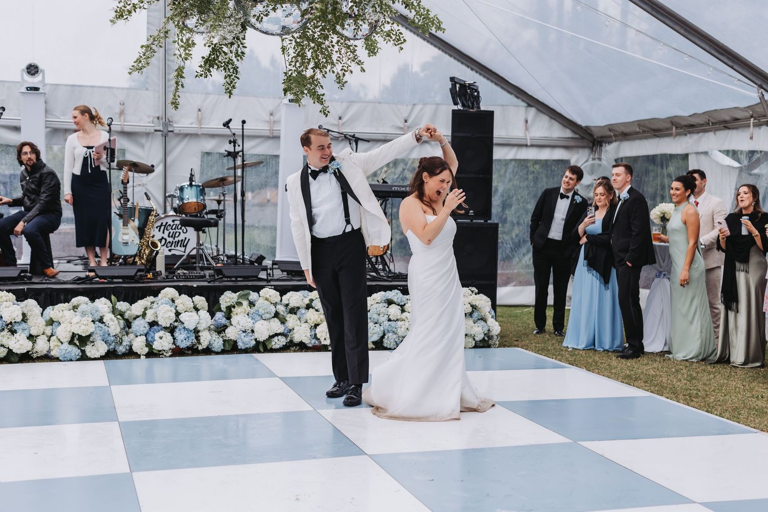 Bride and groom share first dance on black and white checkered dance floor with live band performing behind them.