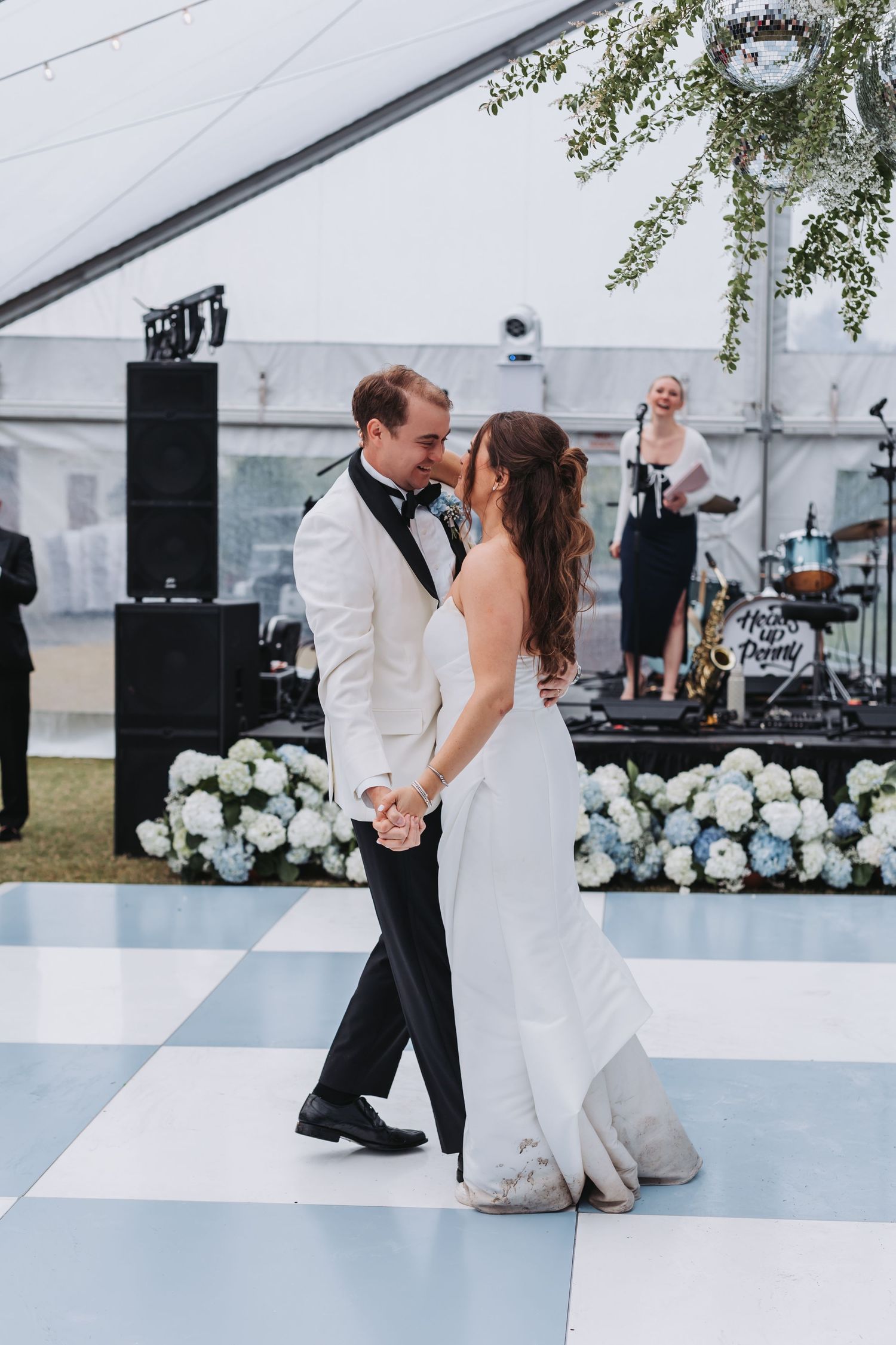 Bride and groom share a romantic first dance kiss on a checkered floor under a floral chandelier.