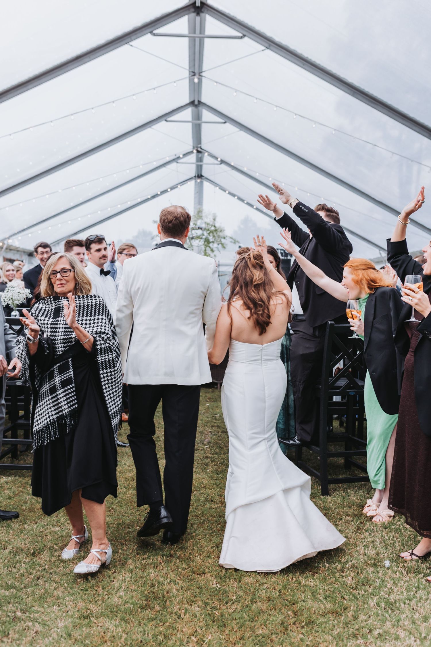 Bride and groom walking through cheering guests under a clear tent during their wedding reception grand entrance.