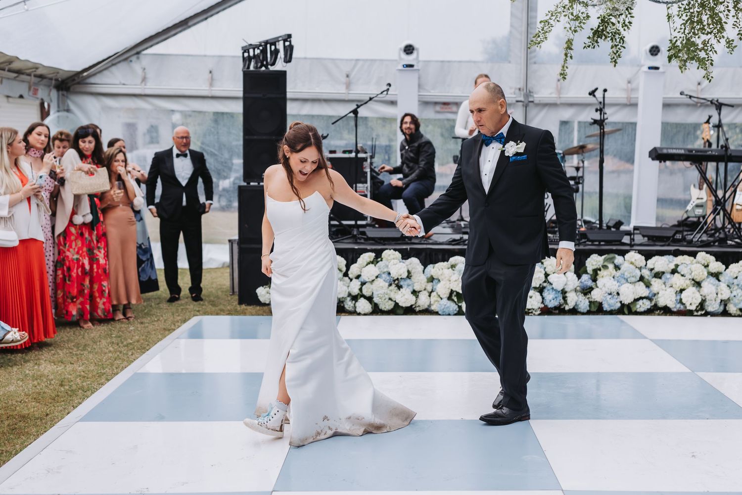 Bride dances with father on checkered dance floor surrounded by guests at elegant outdoor wedding reception.