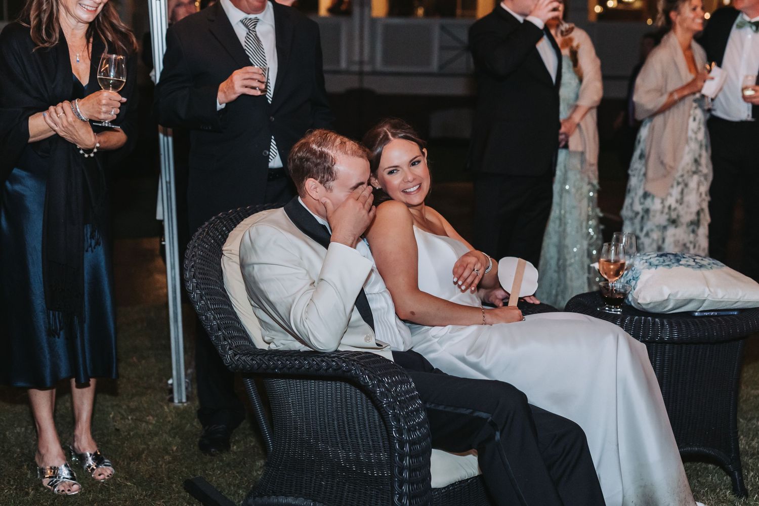 Bride and groom share a joyful moment seated together at outdoor wedding reception.