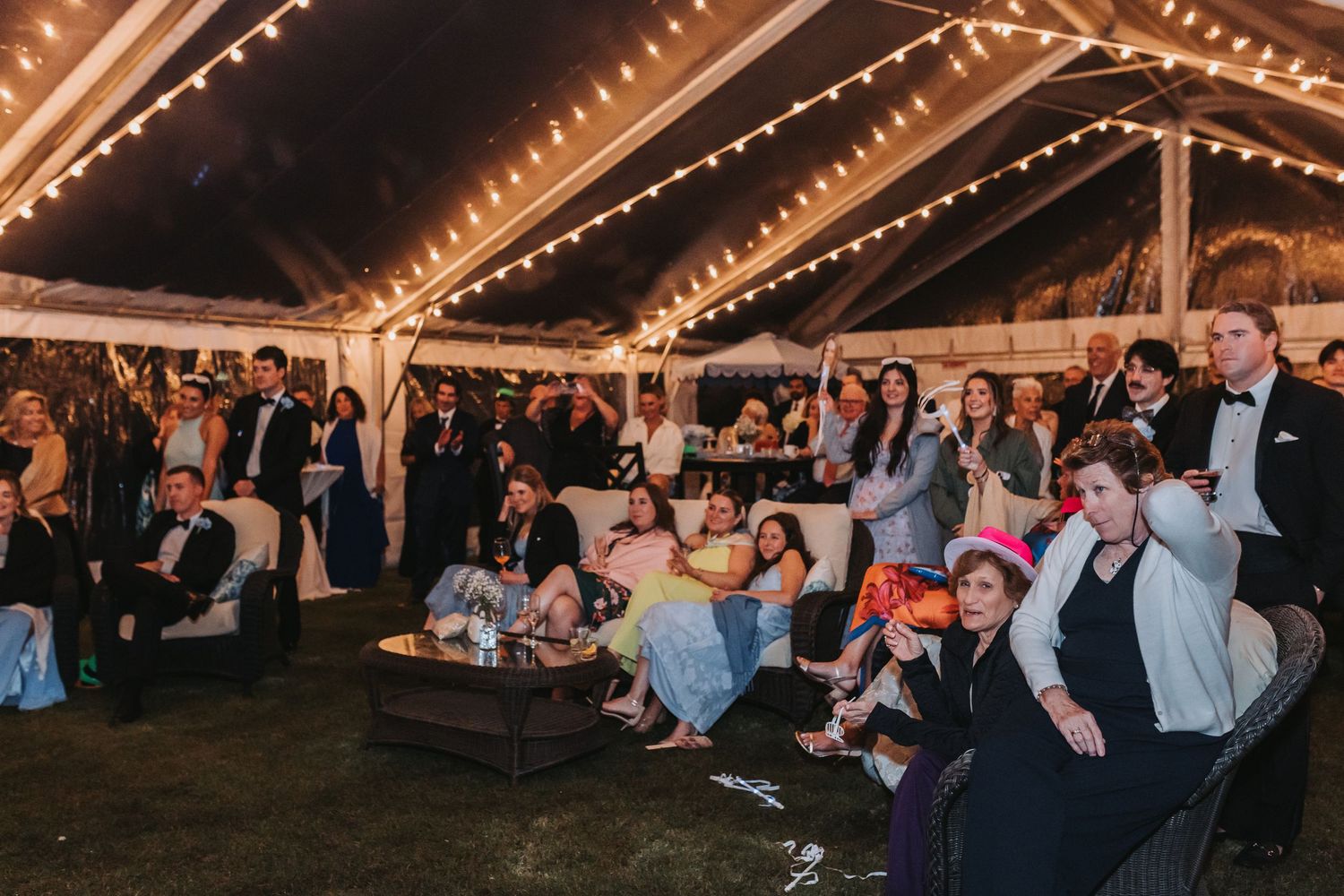 Wedding reception guests gathered under a festive tent with string lights enjoying the evening celebration.