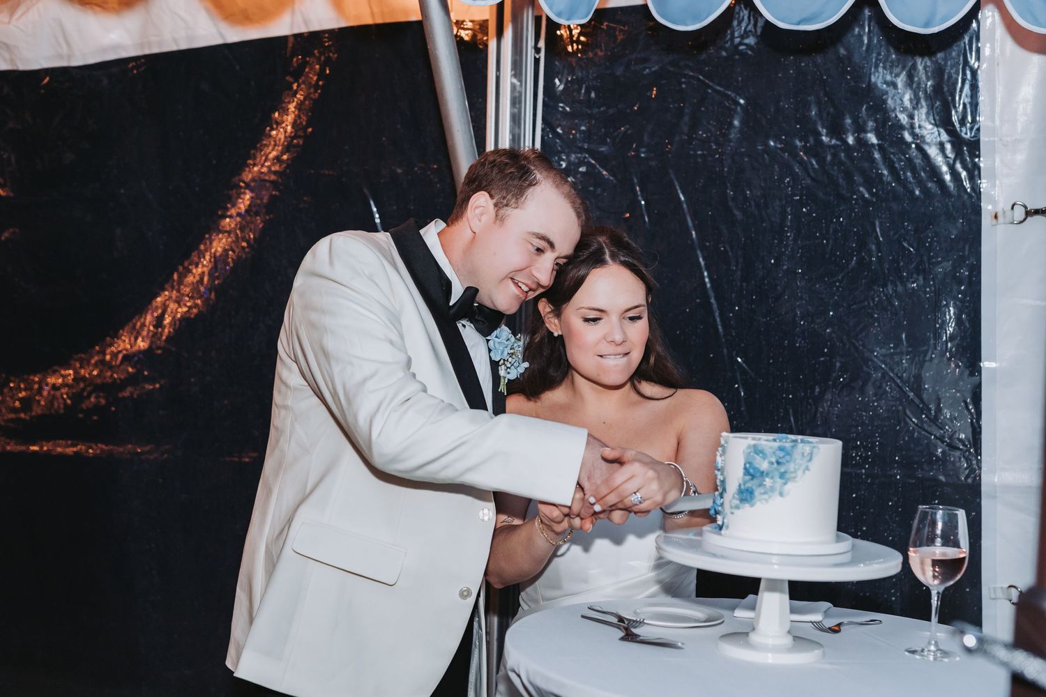 Bride and groom cutting their elegant white wedding cake together at a tented reception.