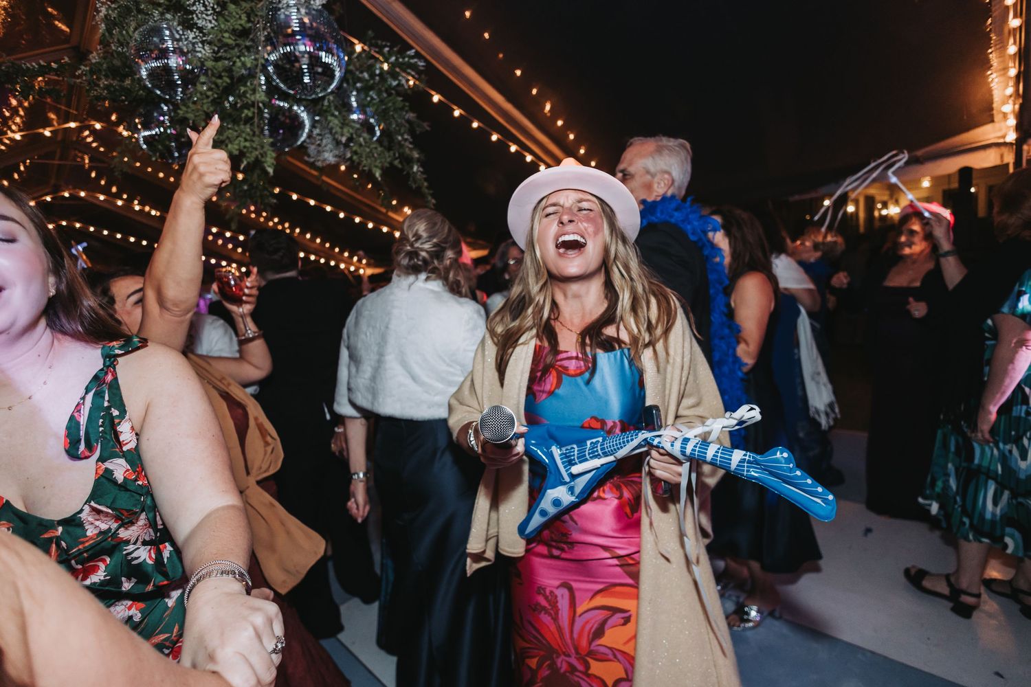 Joyful wedding guest laughing and dancing at lively outdoor evening reception under string lights.
