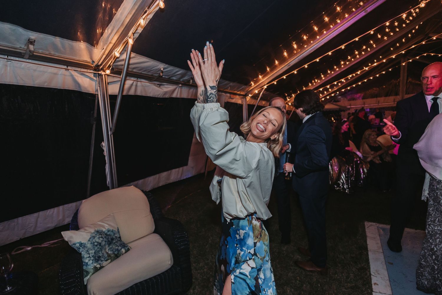 Guest in casual attire dances energetically at outdoor wedding reception under string lights at night.
