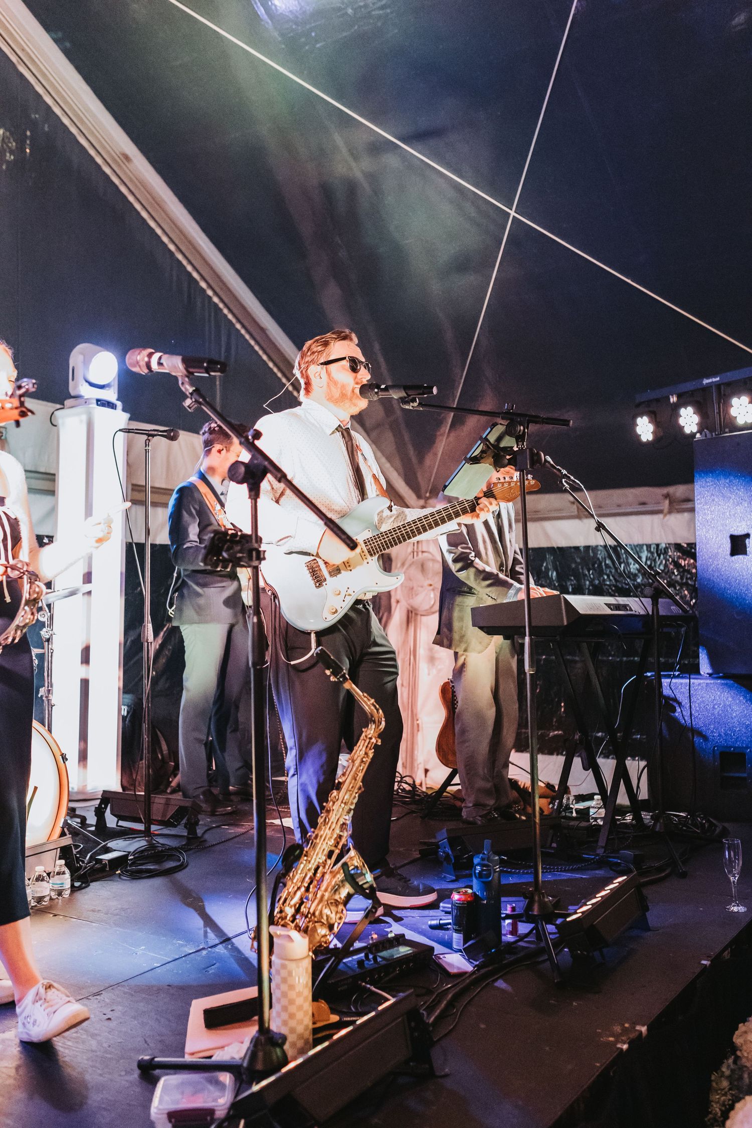 Live wedding band performing on stage with guitarist and saxophone under dramatic stage lighting.