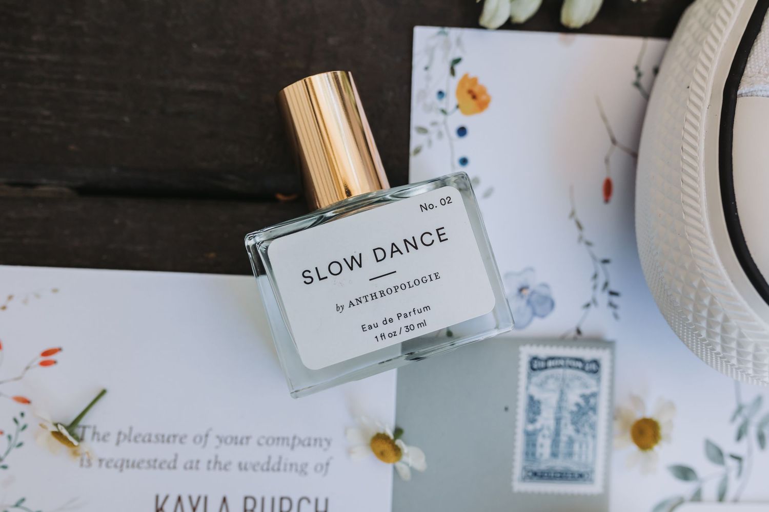 Slow Dance No. 02 Eau de Parfum perfume bottle by Andrée Rouge on a dark wood surface near wedding invitation.