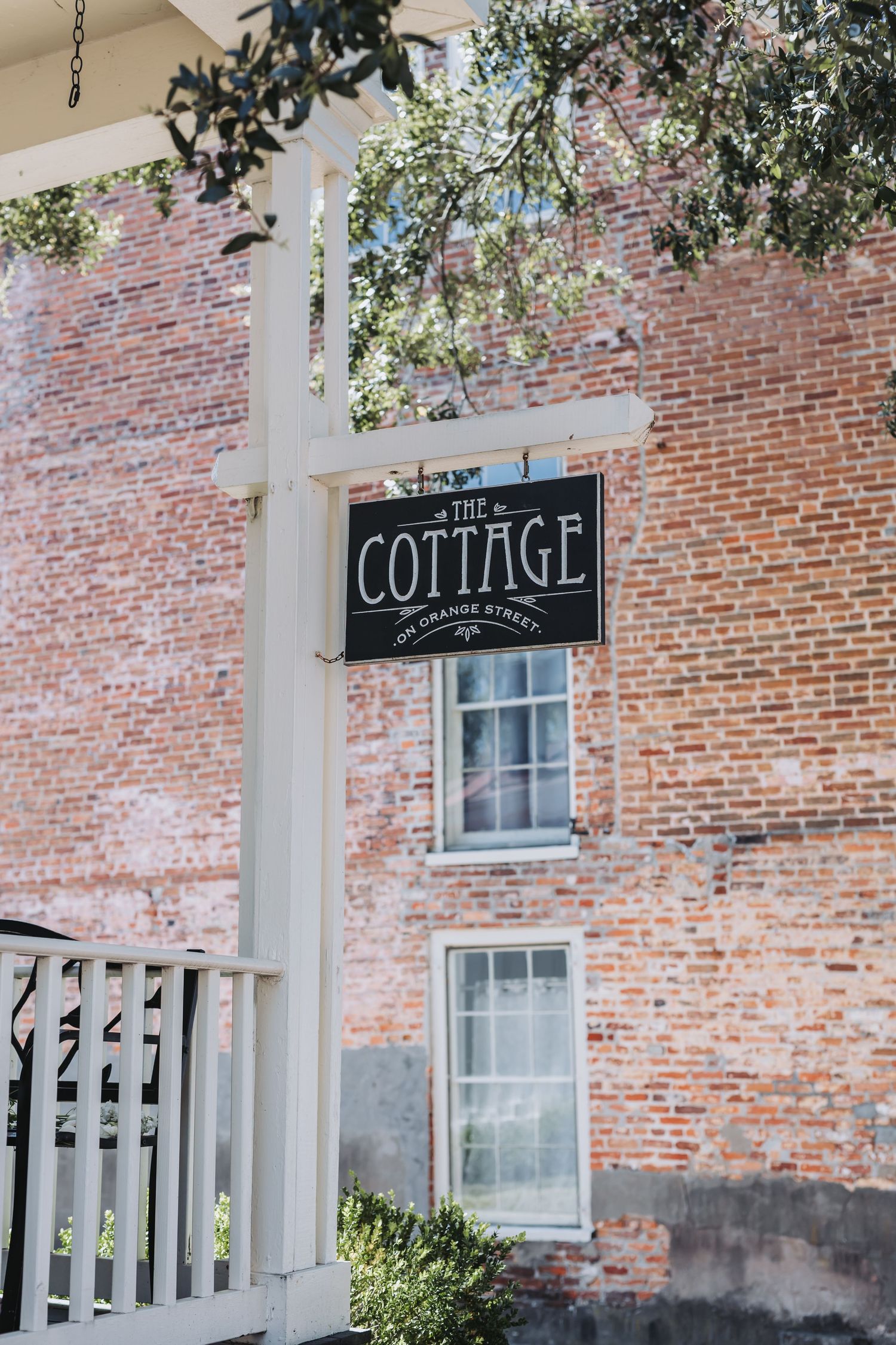 The Cottage sign at 100 Orange Street on white post against rustic brick building facade.