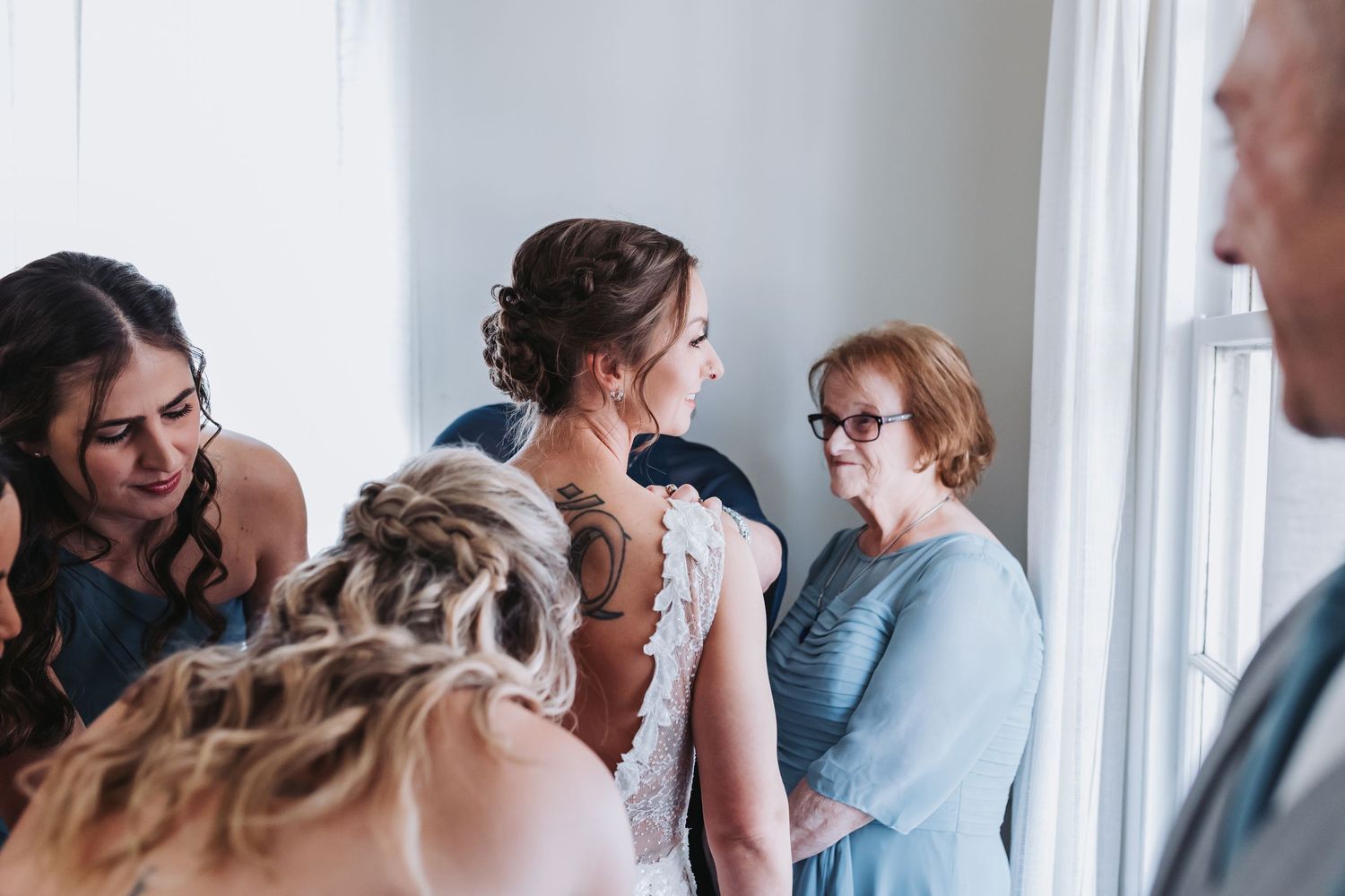 A bride surrounded by bridesmaids and family members helping her prepare for her wedding ceremony indoors.