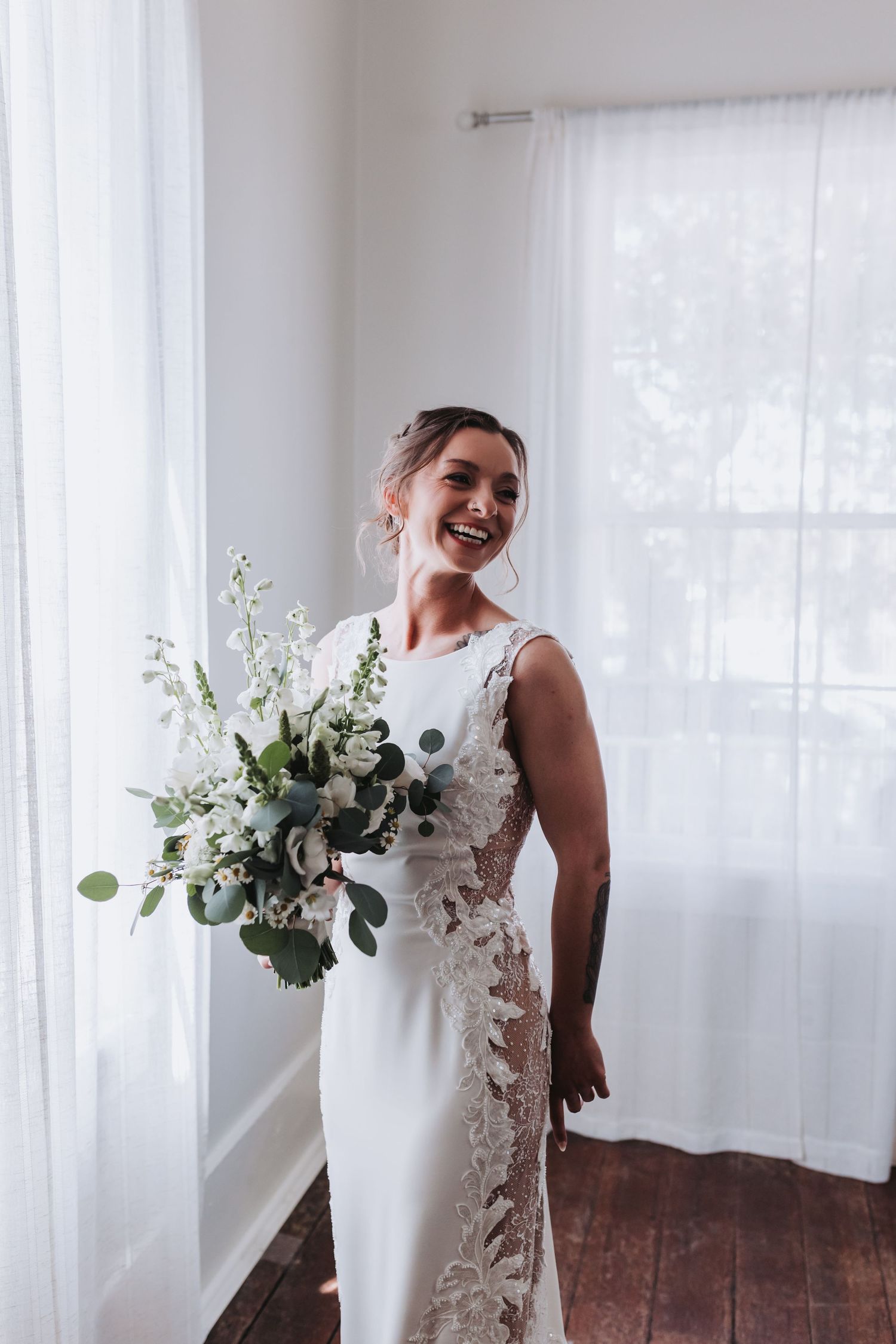 Happy bride in white lace gown holding elegant green and white bouquet.