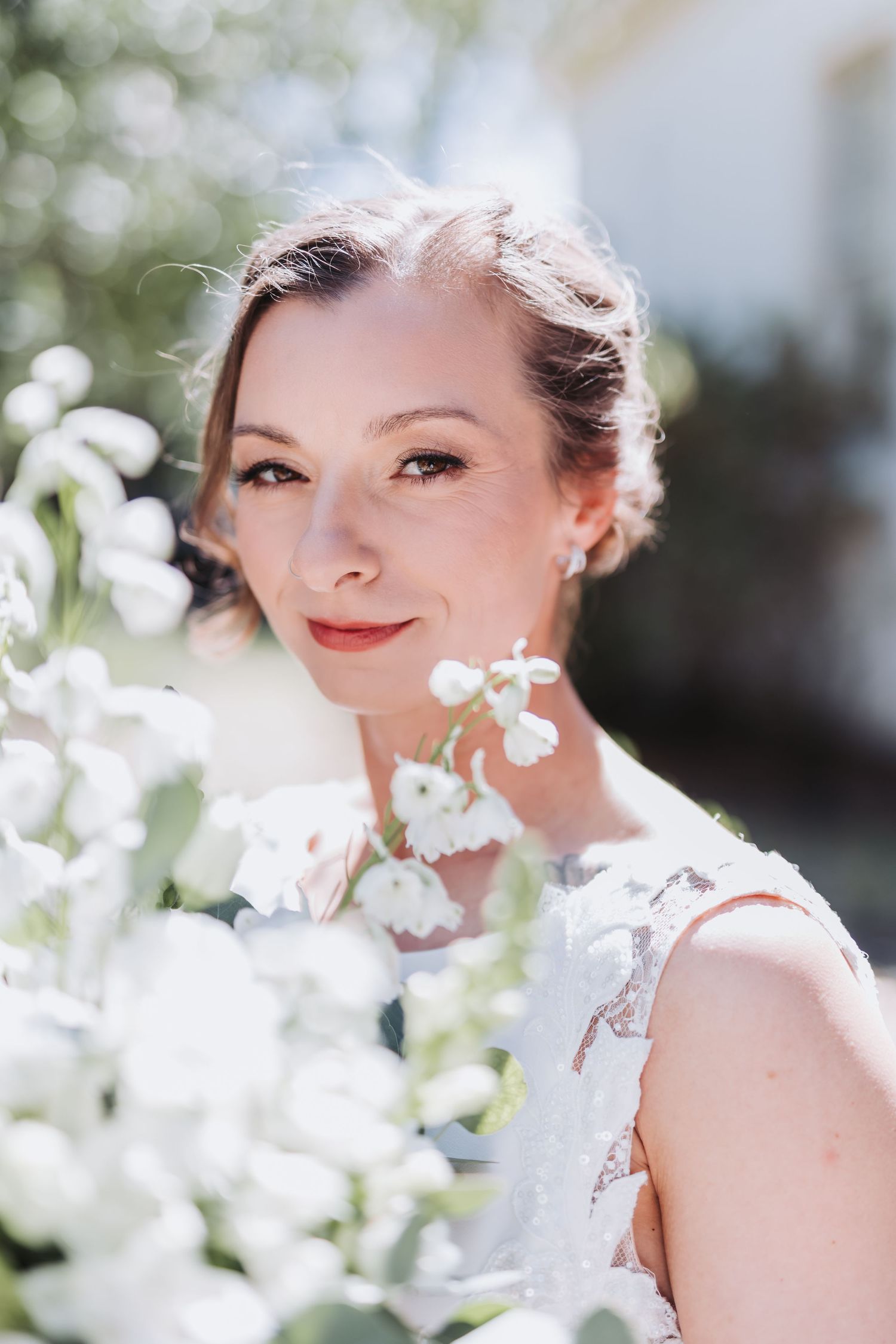 Beautiful bride with updo hairstyle surrounded by white flowers on a sunny wedding day.