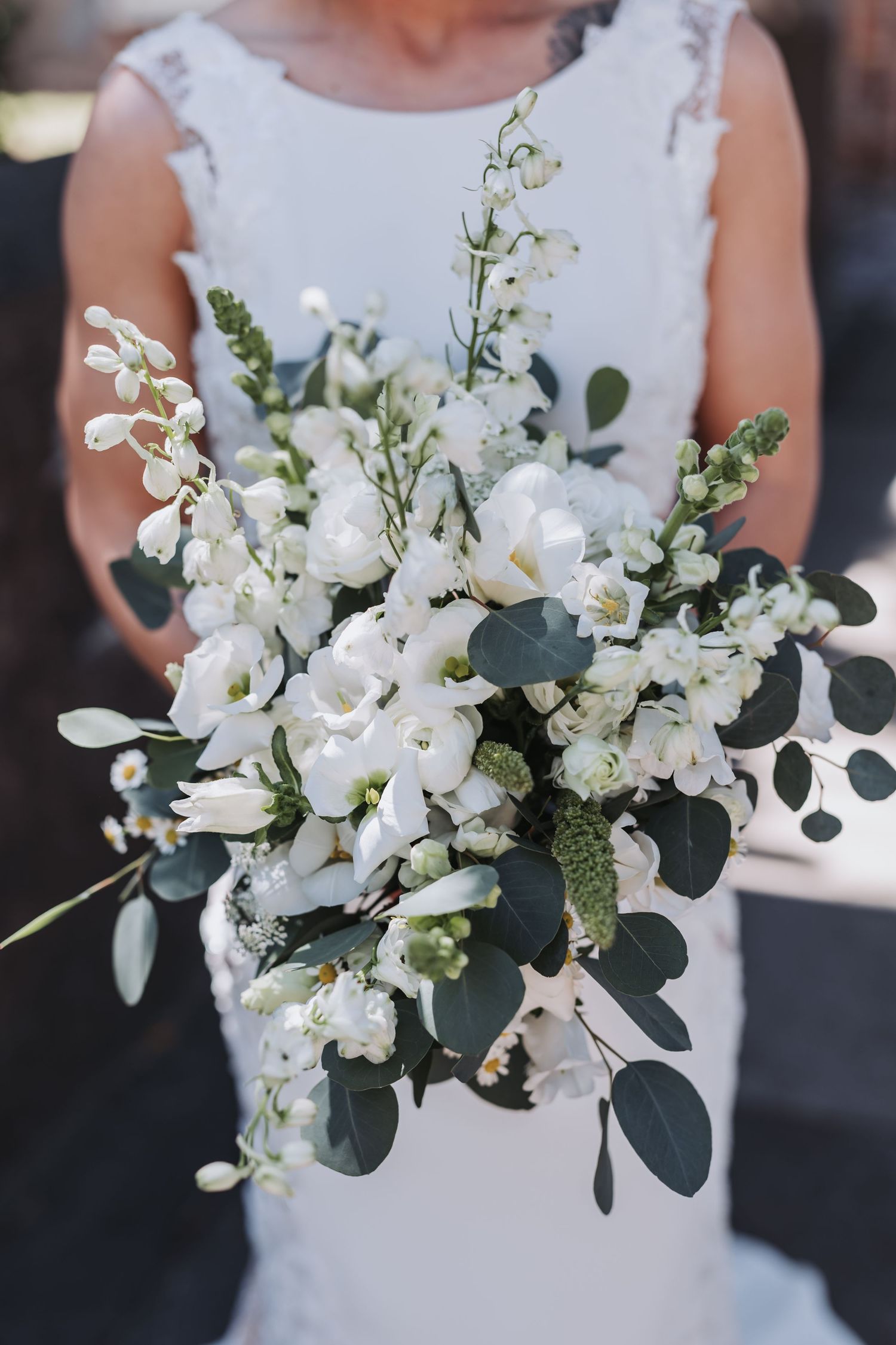 Bride in white lace dress holding a lush bouquet of white freesia, lily of the valley, and eucalyptus greenery.