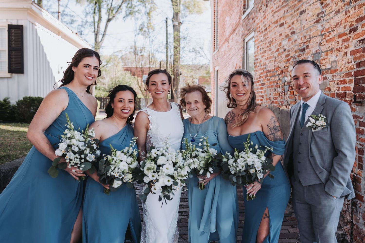 Wedding party posing together with bridesmaids in blue dresses holding white floral bouquets.
