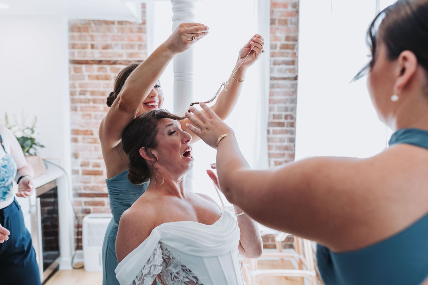 Bridesmaids assisting bride with jewelry and accessories during lively wedding day preparations.