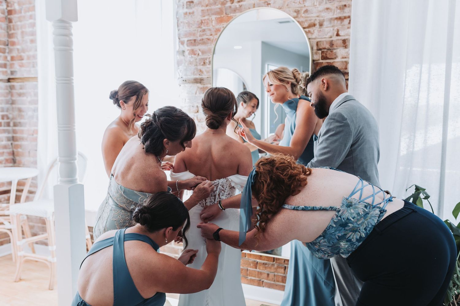 Bridesmaids and family helping bride into wedding gown in rustic venue.