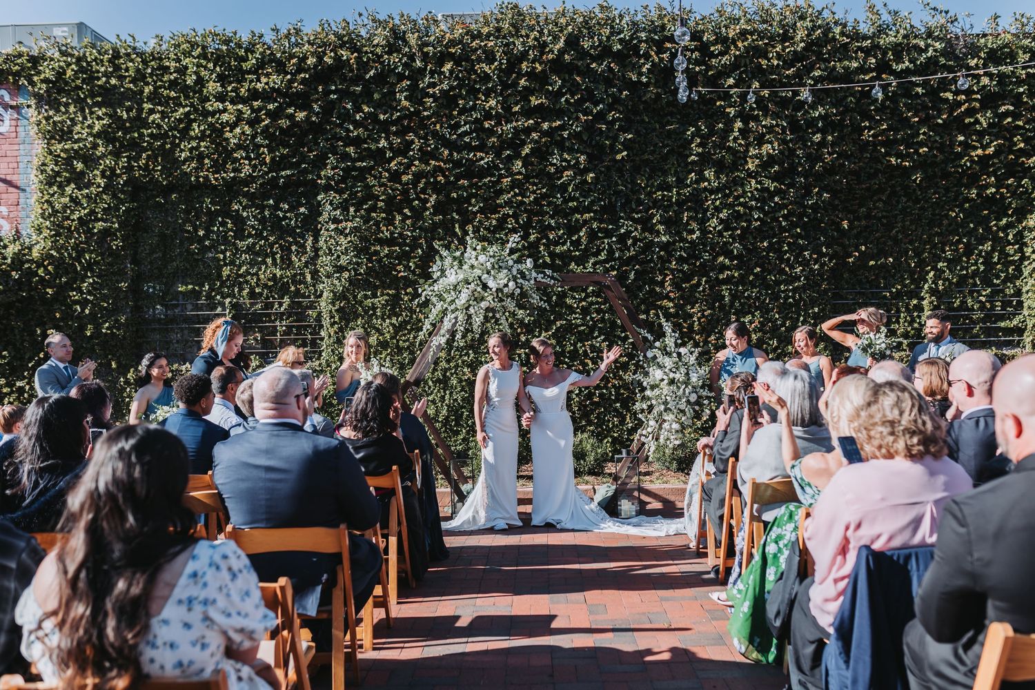 Newlywed couple celebrates with confetti toss while walking back down brick aisle after outdoor wedding ceremony.
