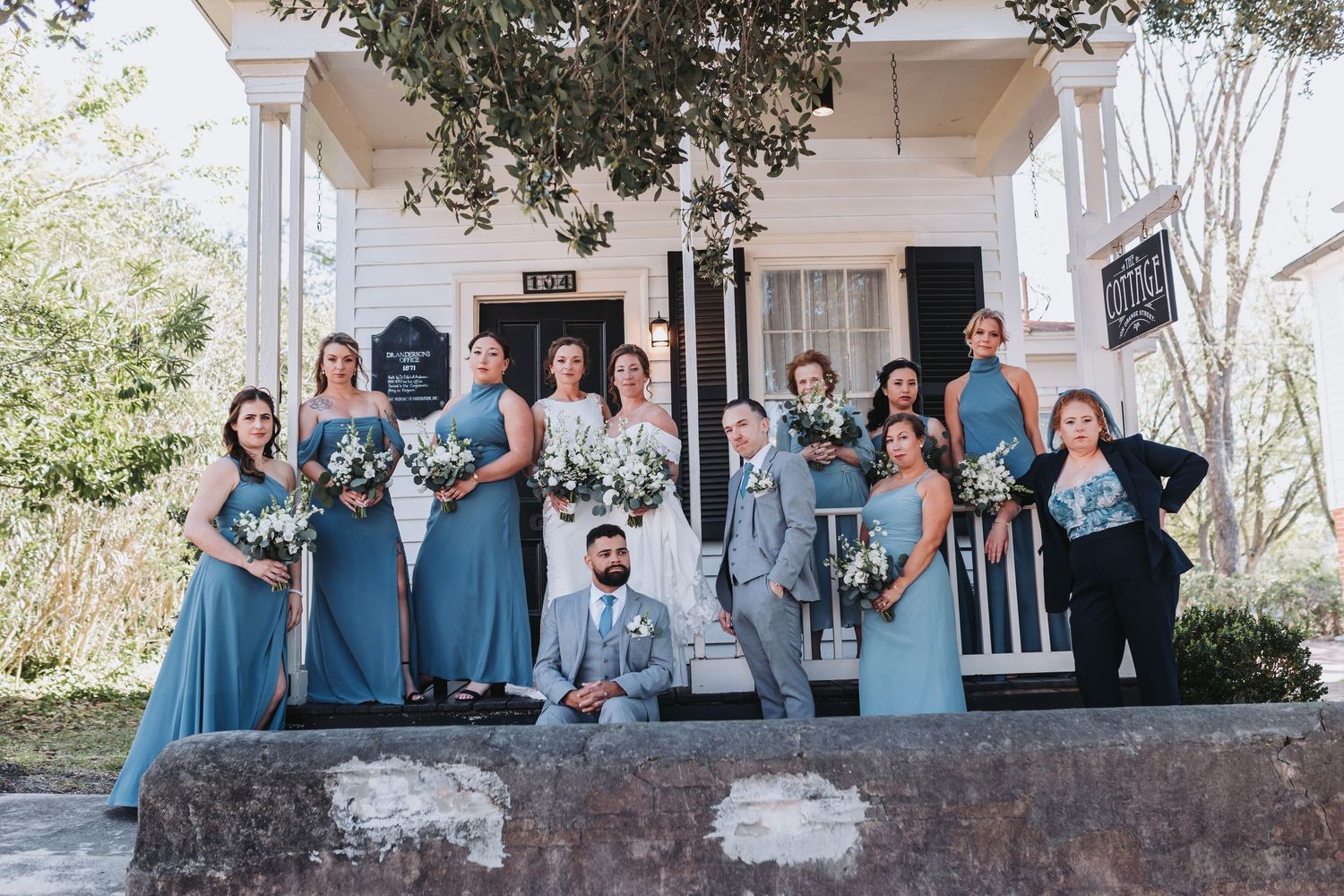 Wedding party in dusty blue dresses and gray suits posing on steps of white historic venue.