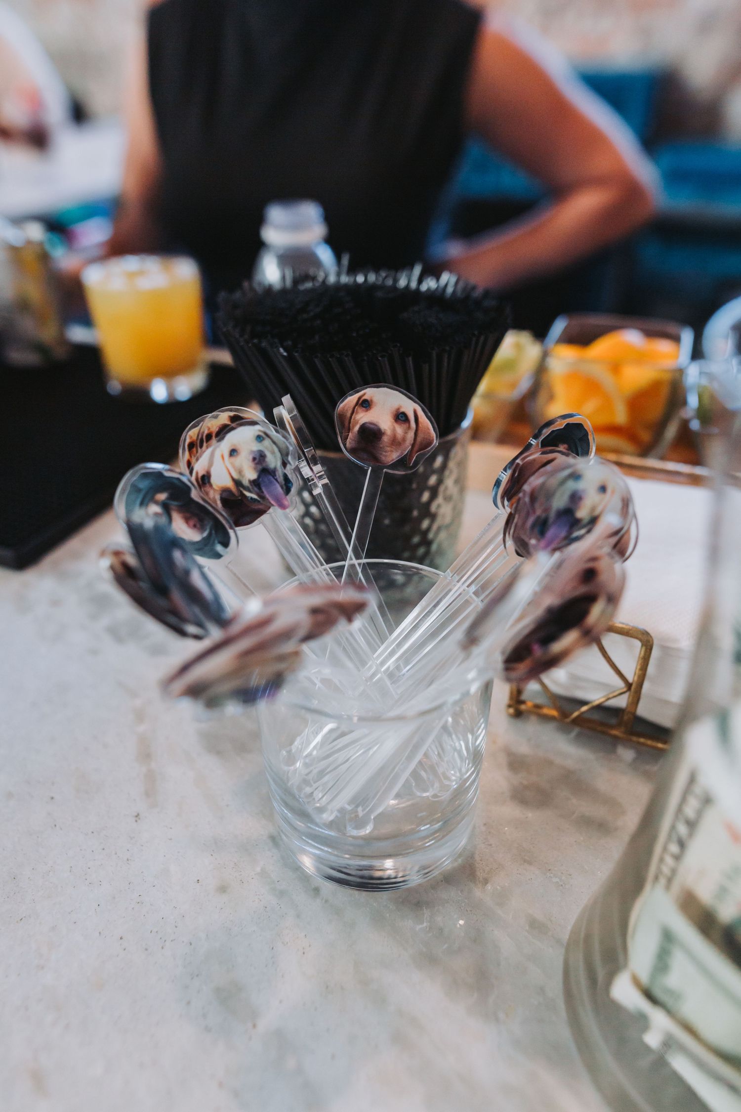 Custom dog portrait cocktail stirrers displayed in a glass at a wedding bar with drinks in the background.