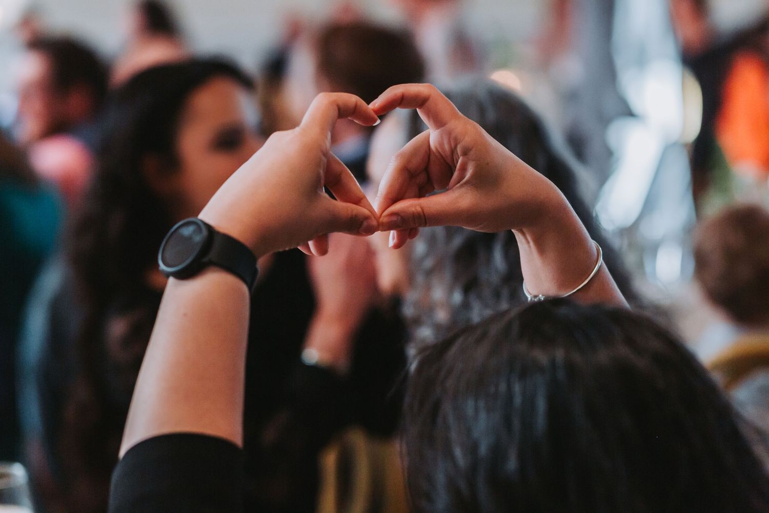 Person making a heart shape with their hands at a festive wedding celebration.
