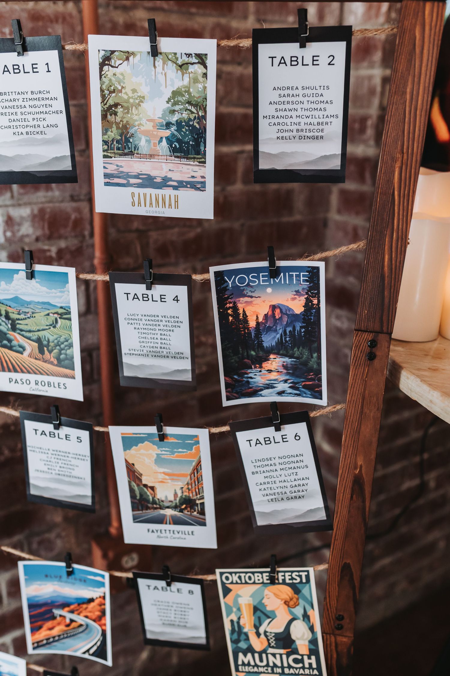 Travel poster themed wedding seating chart displayed on wooden frame with twine and clothespins at rustic brick venue.