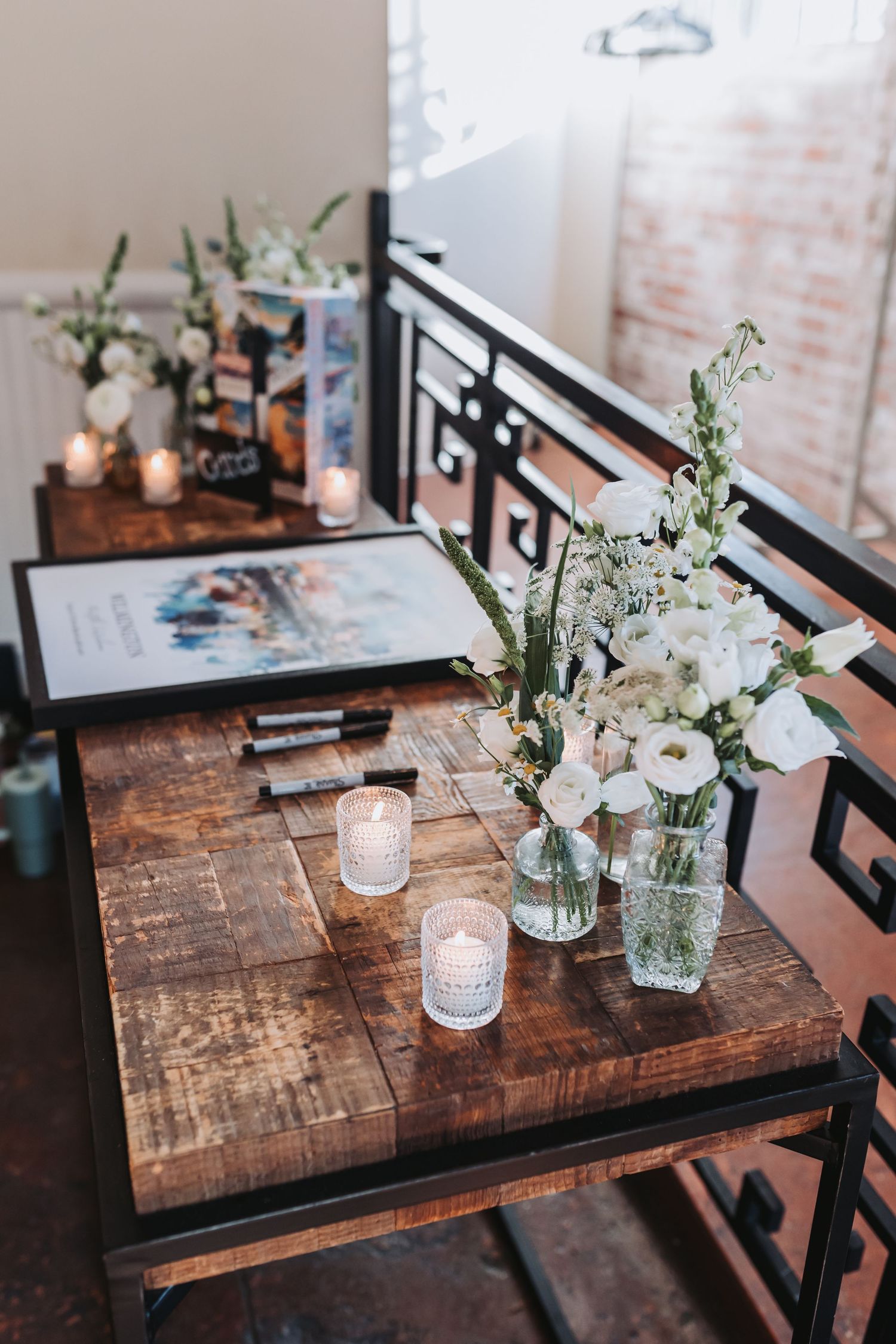 Rustic wooden wedding guest book table with white floral arrangements, candles, and pens at an elegant venue.