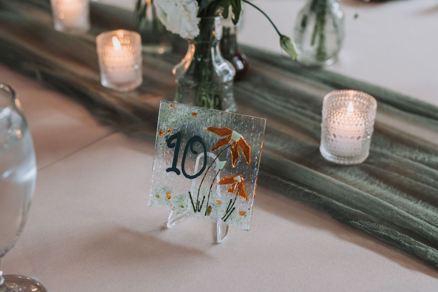 Elegant wedding table number 10 on acrylic stand with pressed flowers, surrounded by candles and floral decor.