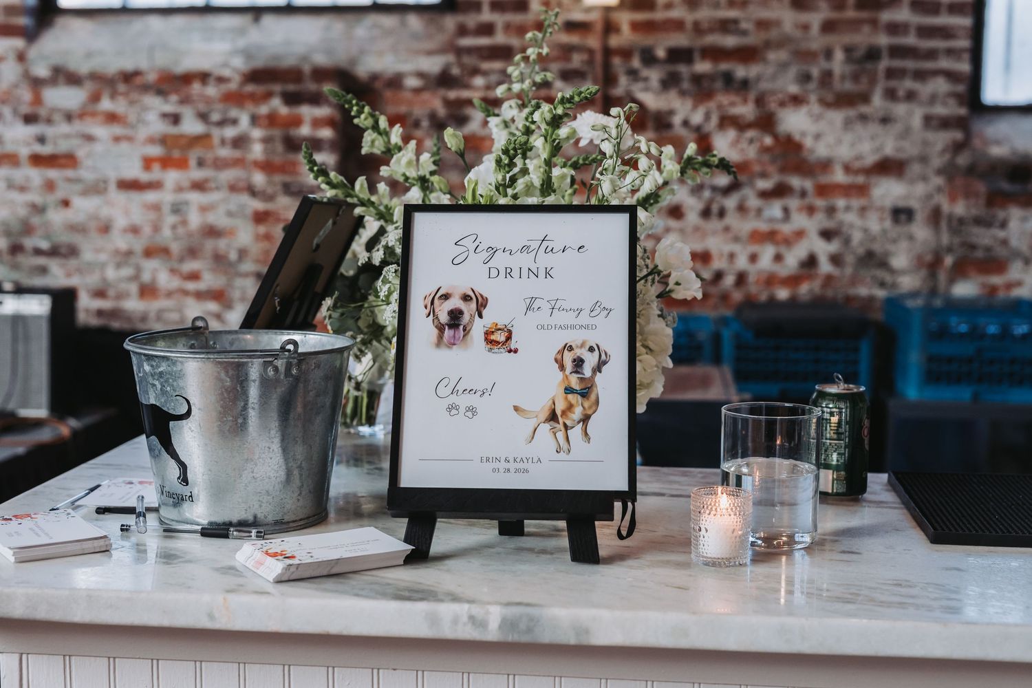 Elegant wedding bar display with signature drink sign featuring illustrated dogs, flowers, and candles.