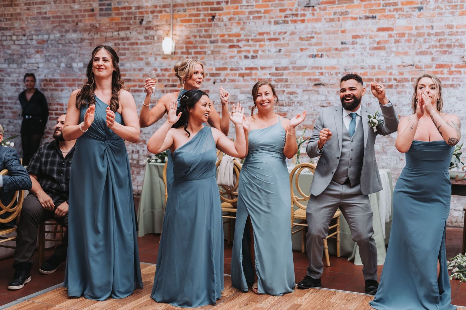 Bridesmaids in blue gowns and groomsman clapping at wedding reception in brick venue.