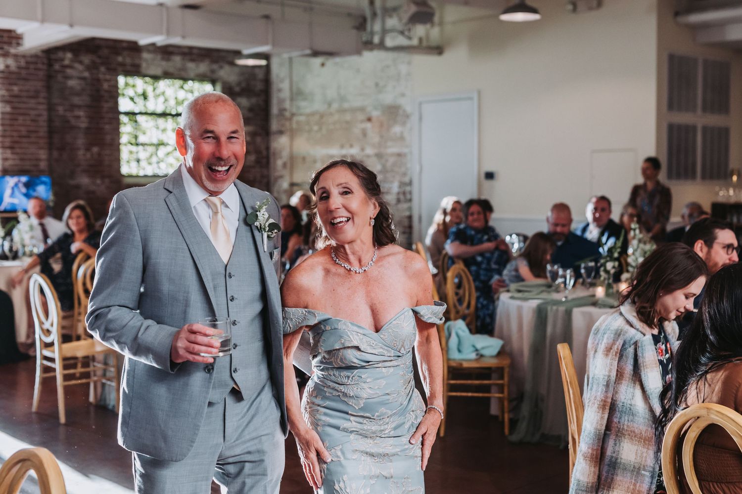 Smiling bride in silver off-shoulder gown and groom in grey suit making grand entrance at wedding reception.