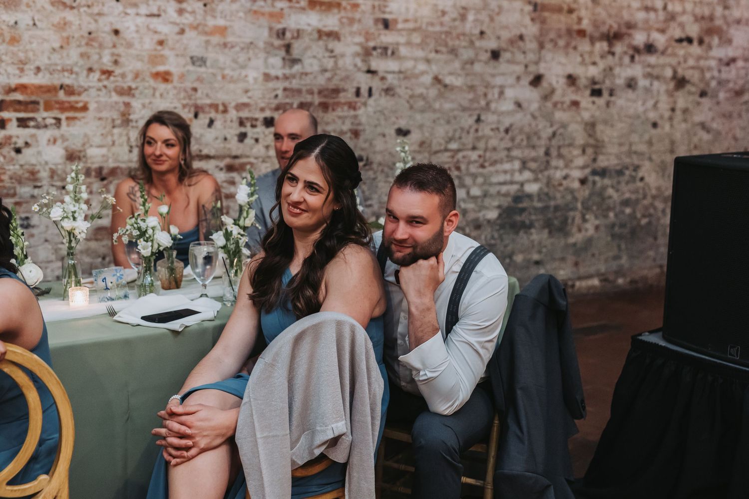 Bridesmaid in blue dress and groomsman smiling together at wedding reception dinner table.