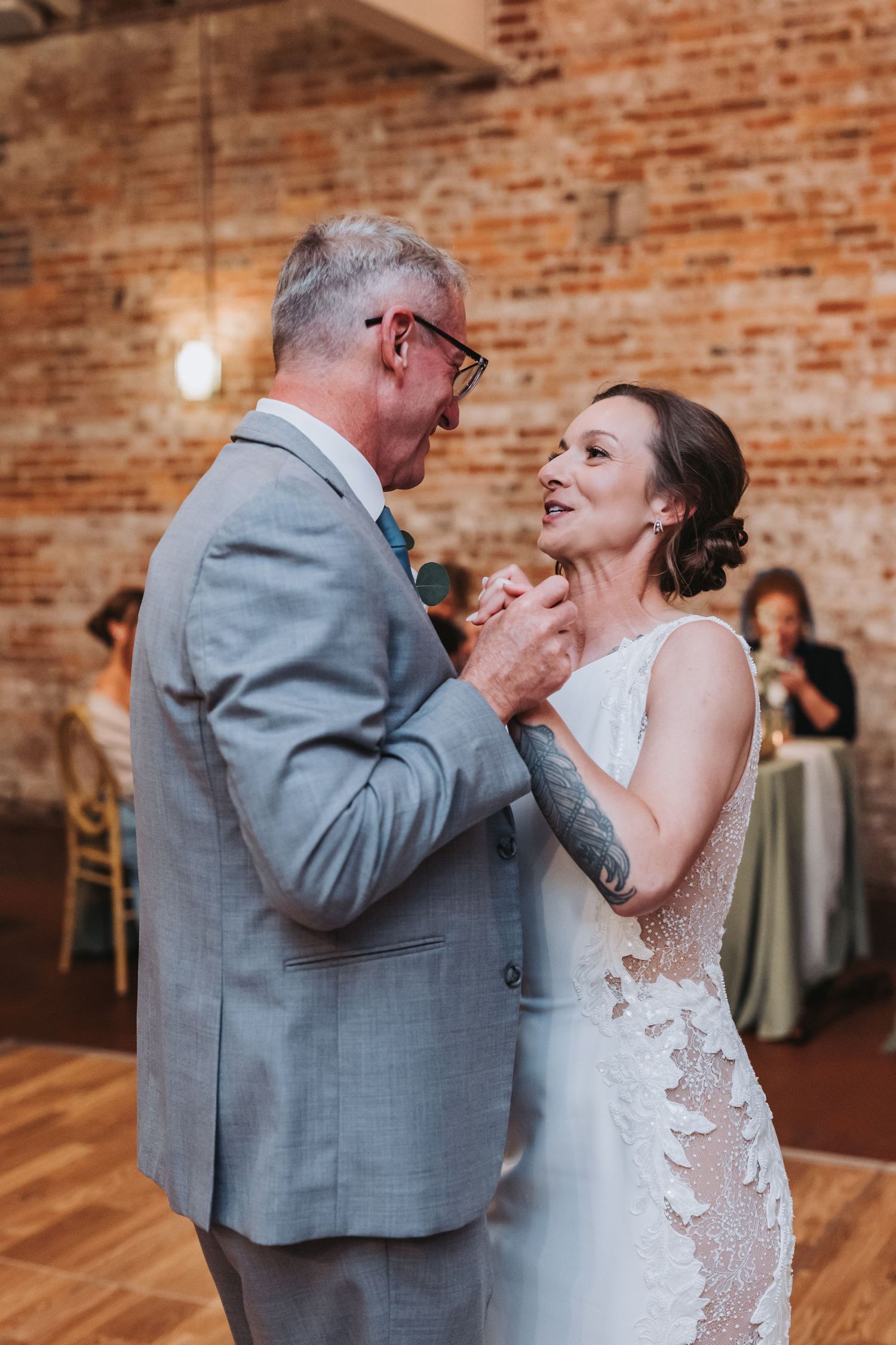 A bride and groom share a romantic first dance in a rustic brick-walled wedding venue.