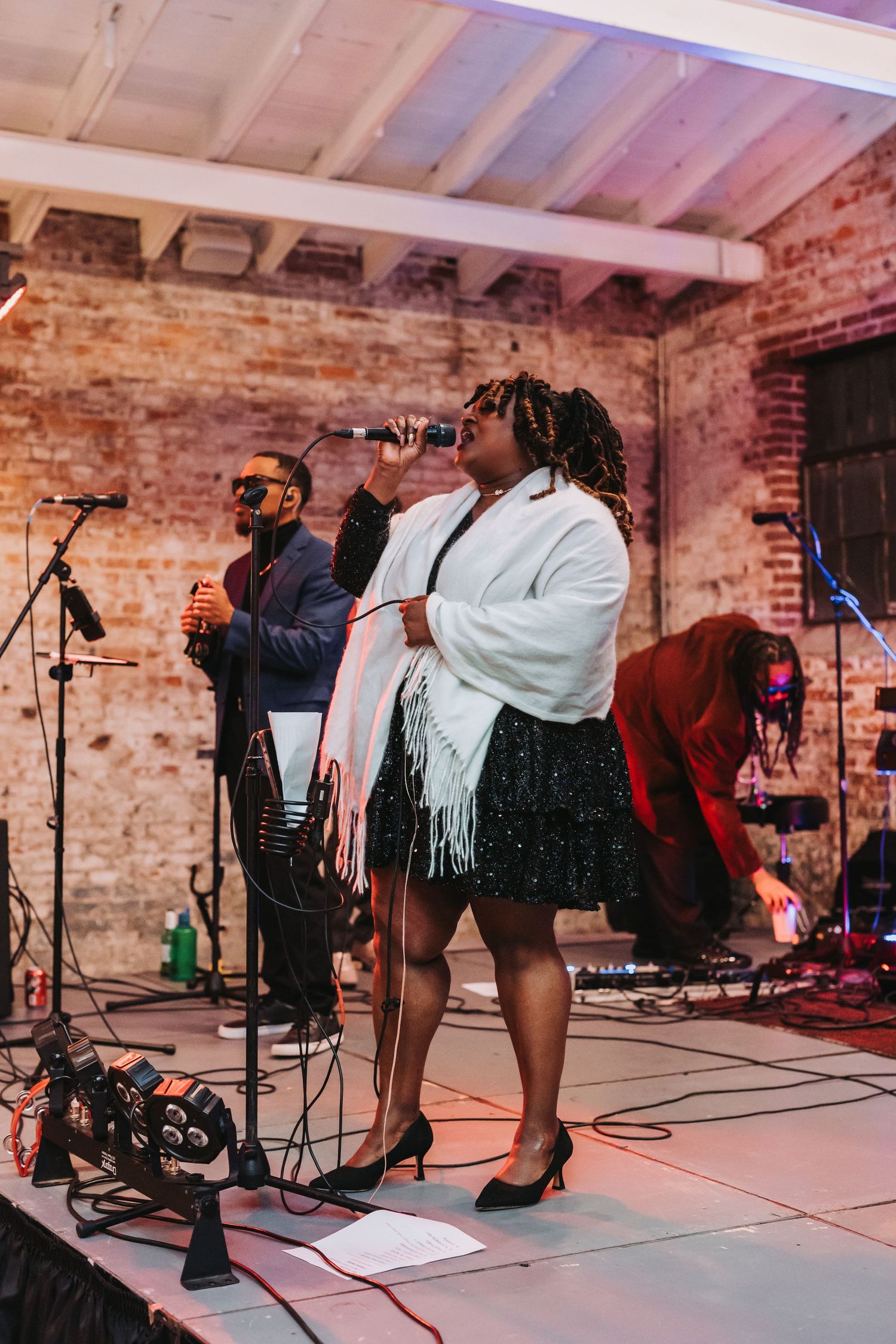Live band performing at wedding reception in rustic brick venue with stage lighting.