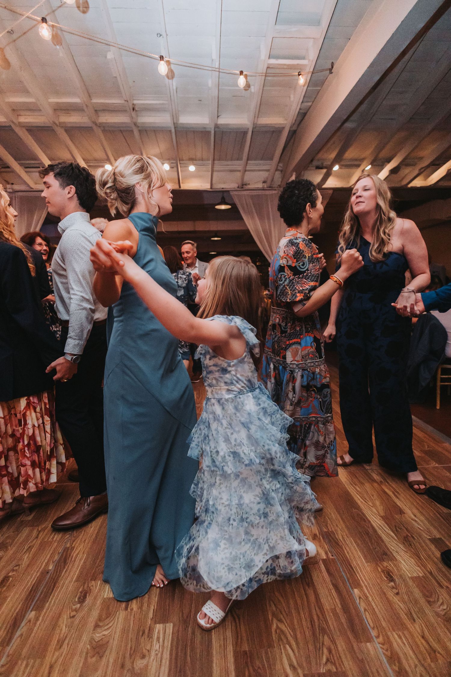 Guests including a young girl in a floral dress dance together at an elegant wedding reception.
