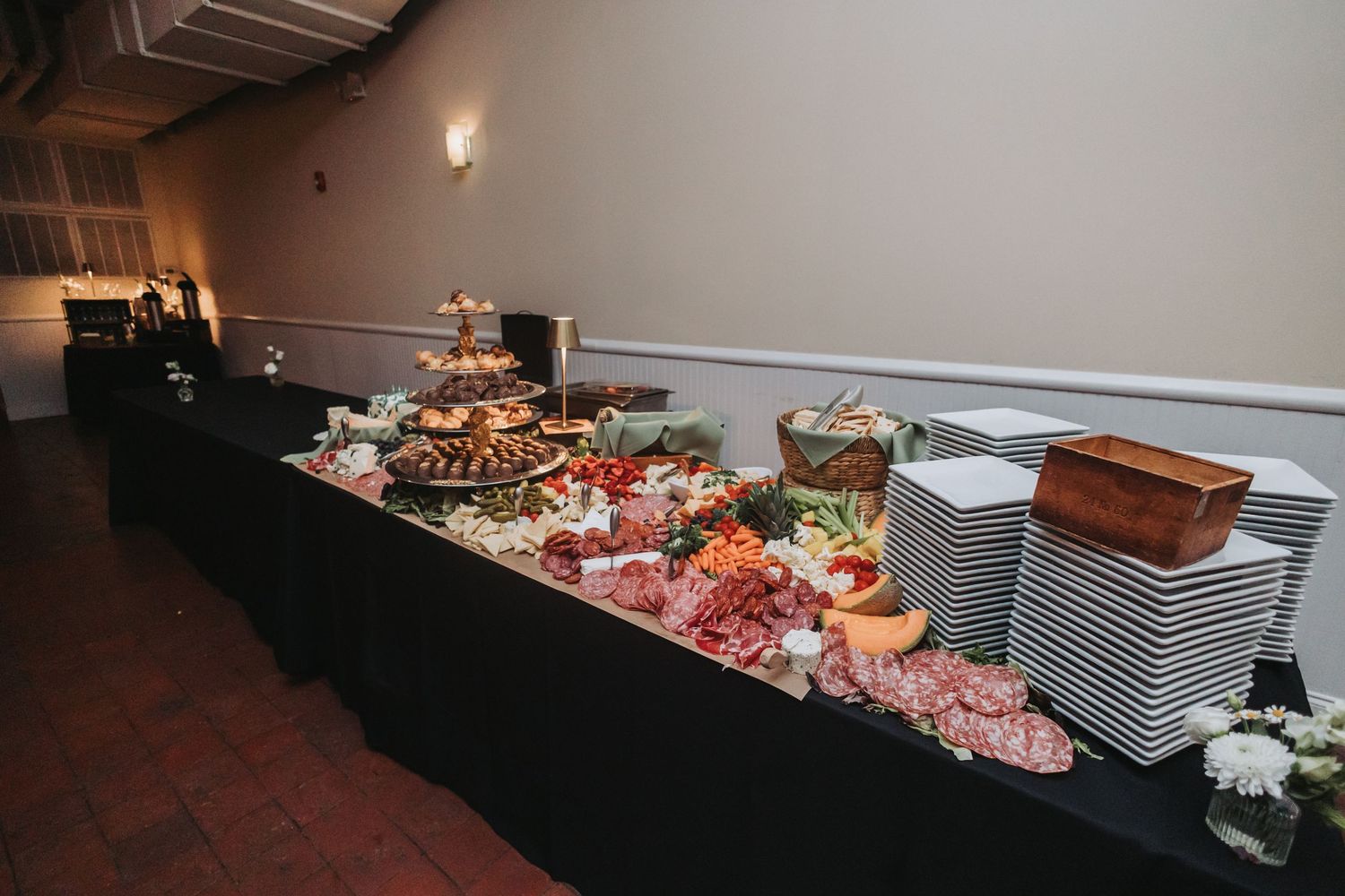 Elegant wedding buffet table with charcuterie, fruits, and stacked white plates.