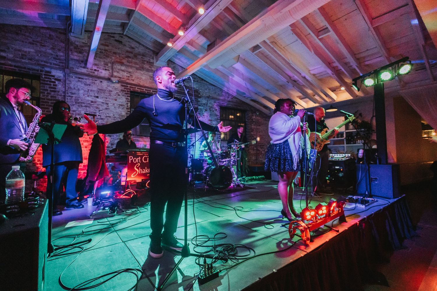 Live band performing on stage in a brick venue with colorful stage lighting during an energetic concert.