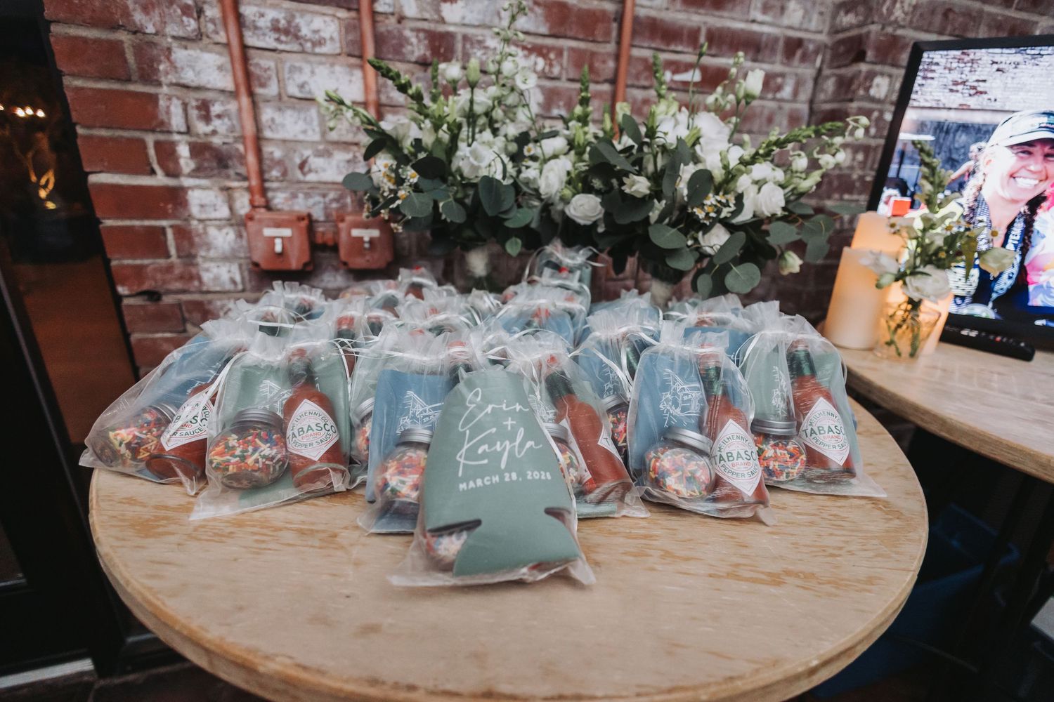 Custom sage green wedding favor koozies with couple's name displayed on a wooden table with floral decor.