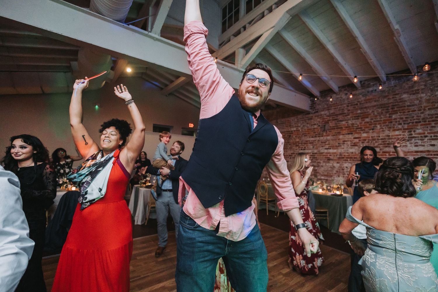 Energetic wedding guest dancing and raising arm at lively reception party on dance floor.