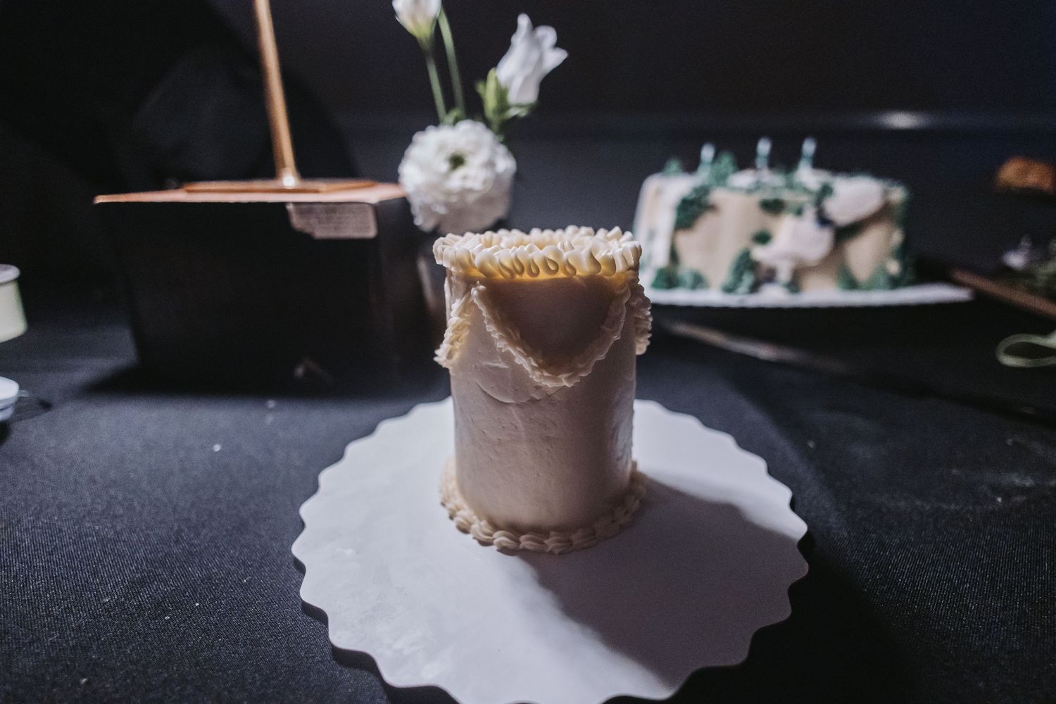 Elegant mini wedding cake with gold trim displayed on a white doily at a reception table.