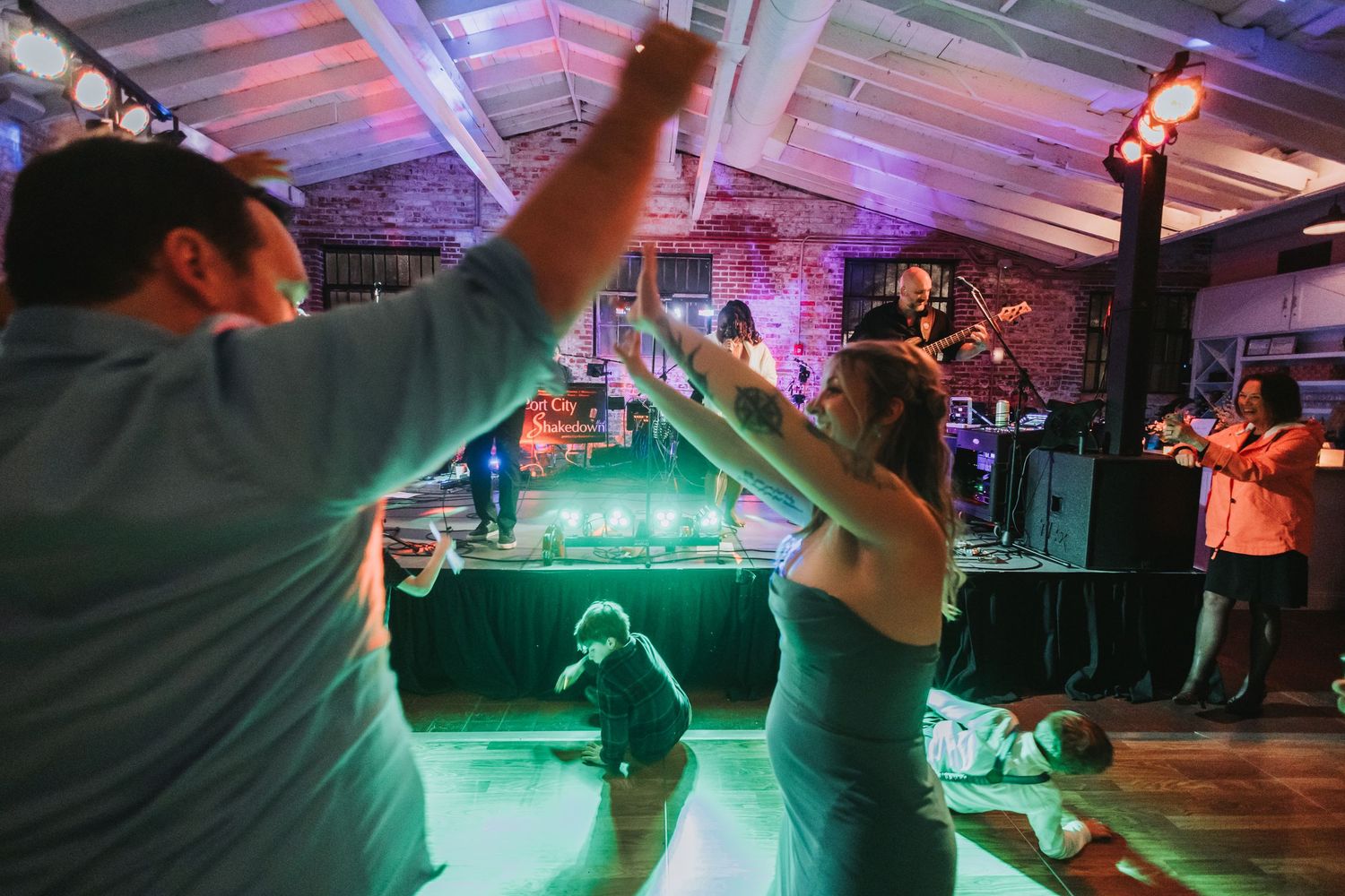Guests dancing energetically at a wedding reception with live band and colorful green stage lighting.